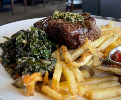 Steak with green salsa, sautéed greens, French fries, and ketchup on a white plate.