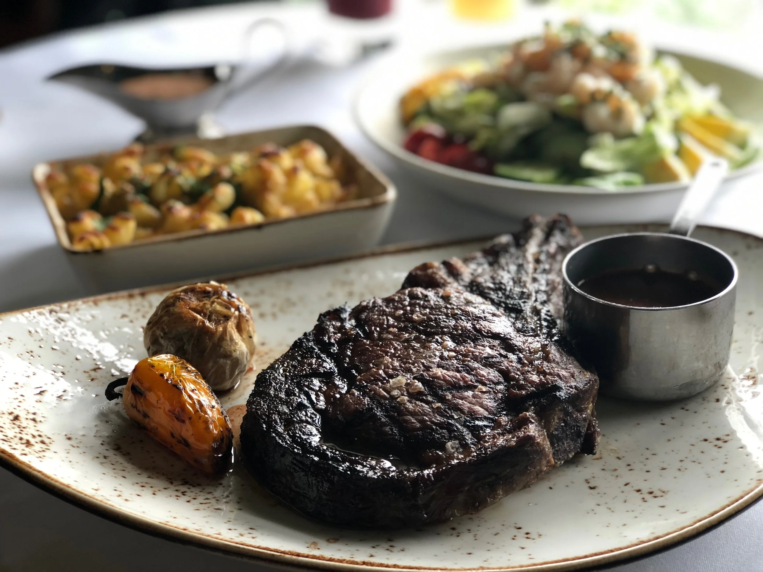 Barbecue ribs served with grilled vegetables including a roasted yellow pepper and a roasted cherry tomato, on a white plate with speckled seasoning.