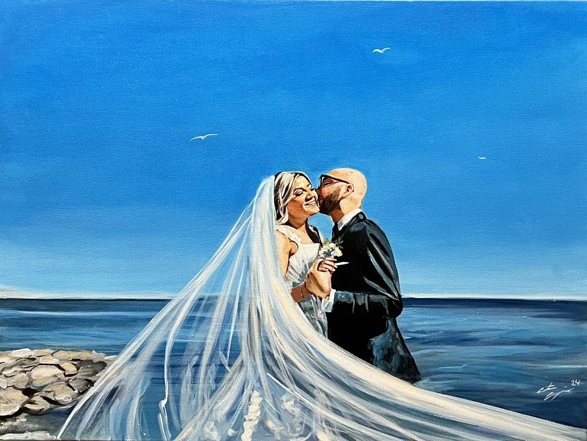 A bride and groom stand close together on a beach, smiling and sharing a kiss. The bride wears a white wedding dress and veil, holding a small bouquet, while the groom is dressed in a black suit and glasses. The lake and a few birds are in the back. 