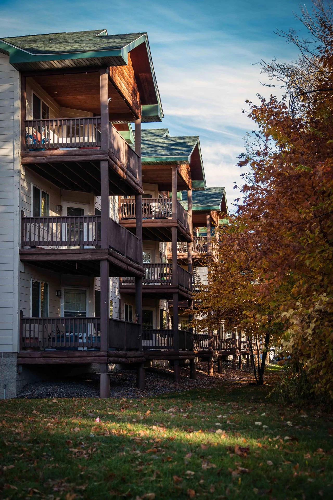 Multiple floors of an apartment building with balconies, surrounded by trees with autumn leaves.
