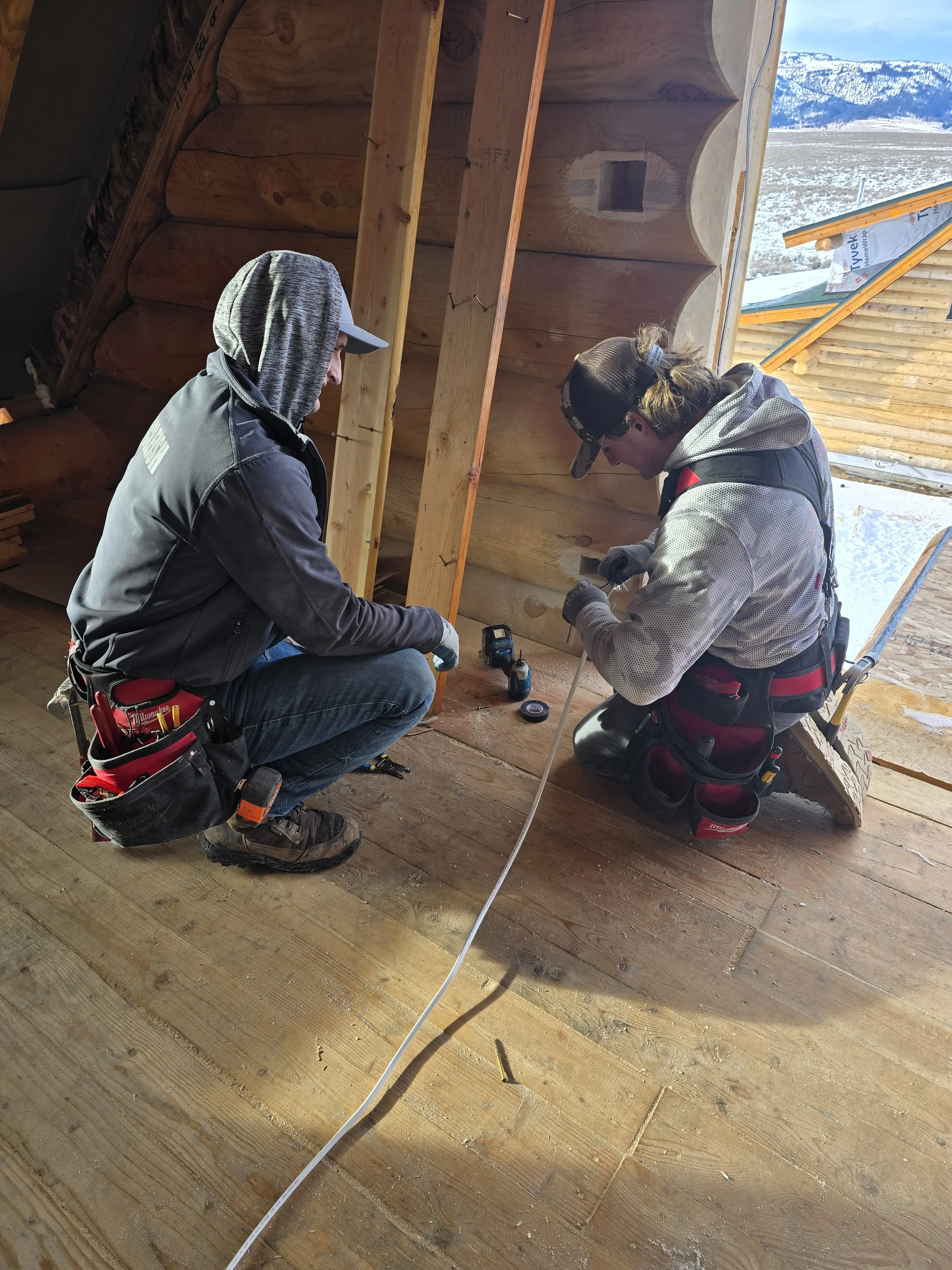 Two construction workers inside a partially built wooden structure working with tools and equipment.