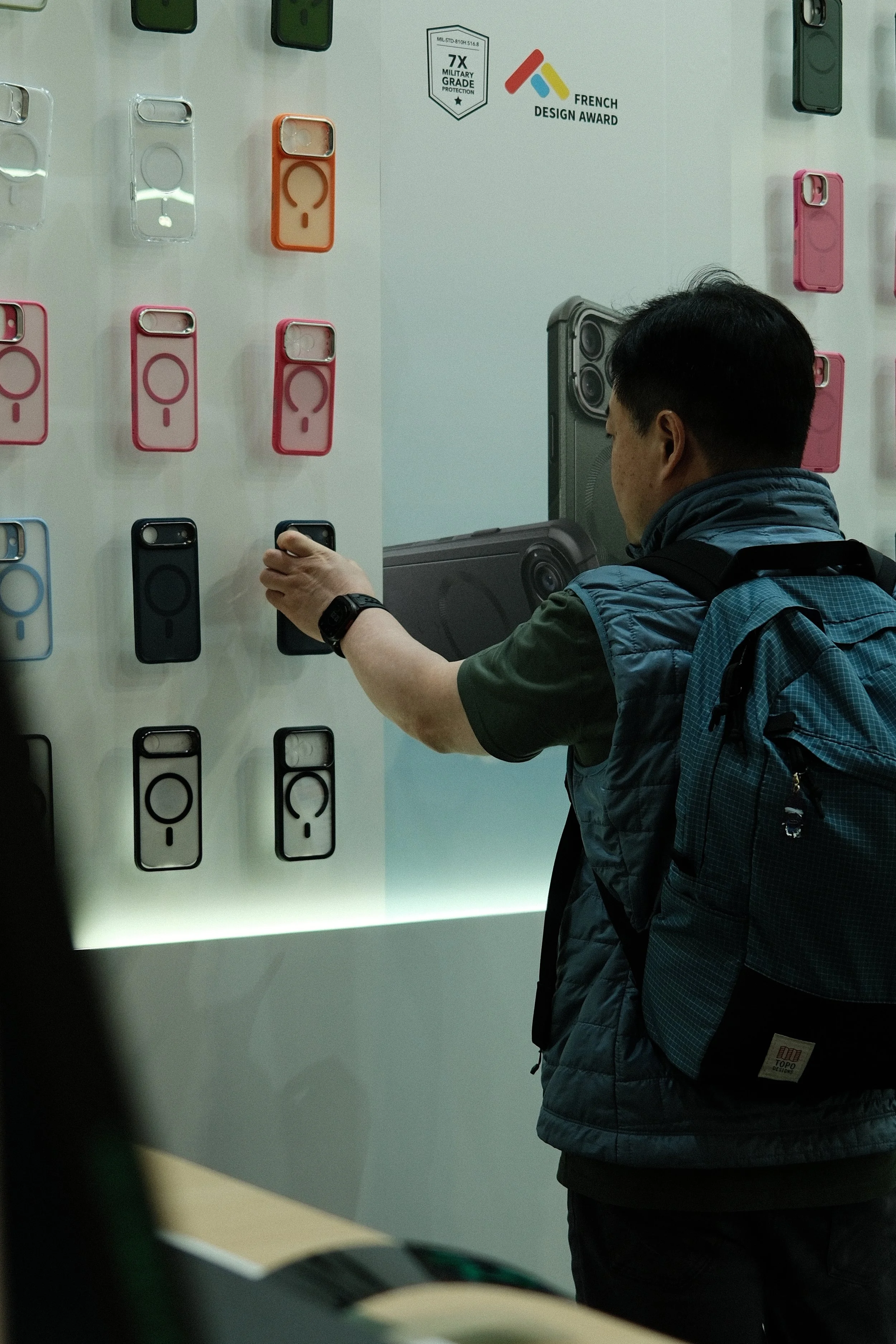 A man shopping for phone cases at a store, trying out a black case on display.