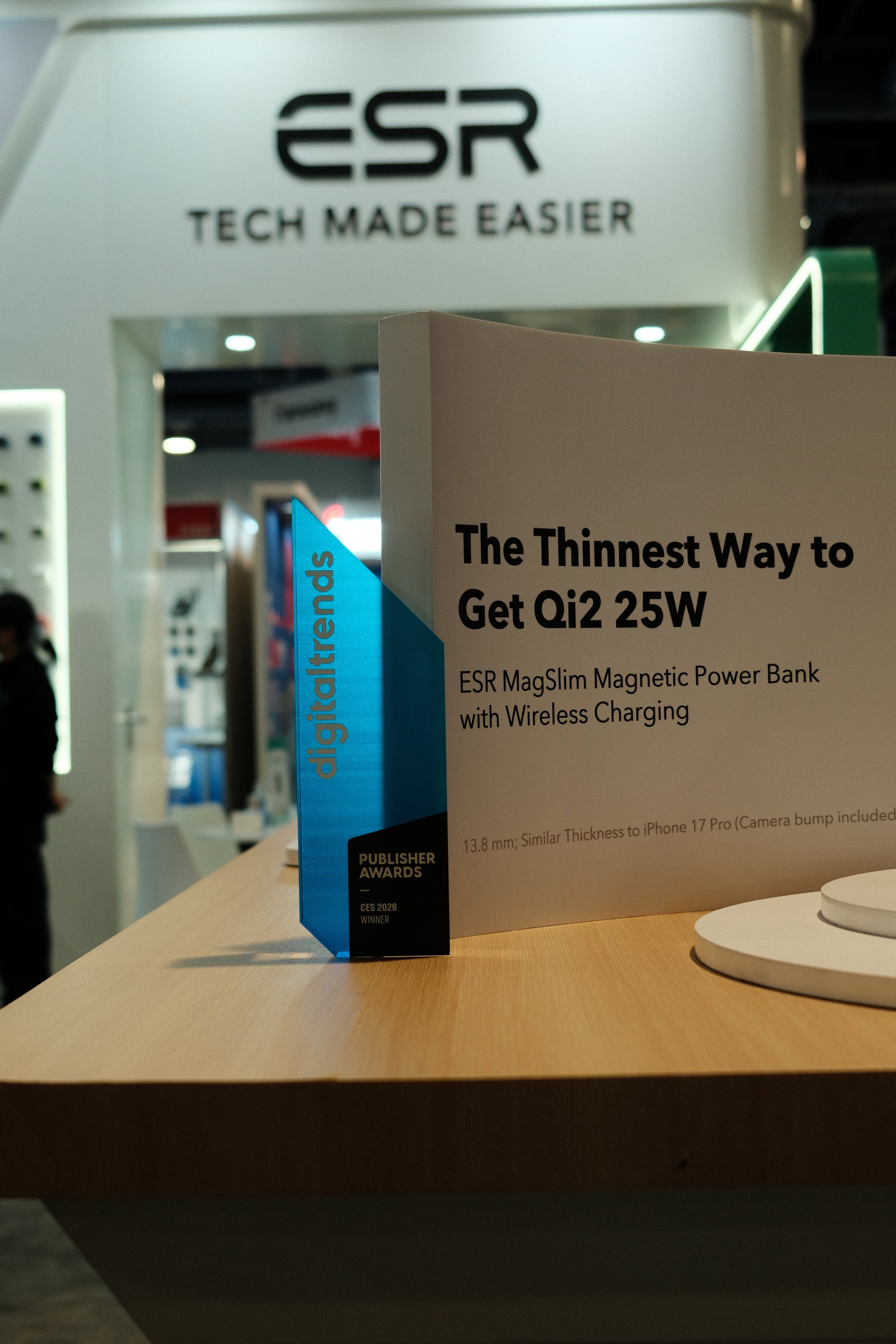 A display at a technology event showcasing the ESR MagSlim Magnetic Power Bank with wireless charging. The display is on a wooden surface with a sign that reads "The Thinnest Way to Get Qi2 25W" and mentions similar thickness to an iPhone 17 Pro. In 