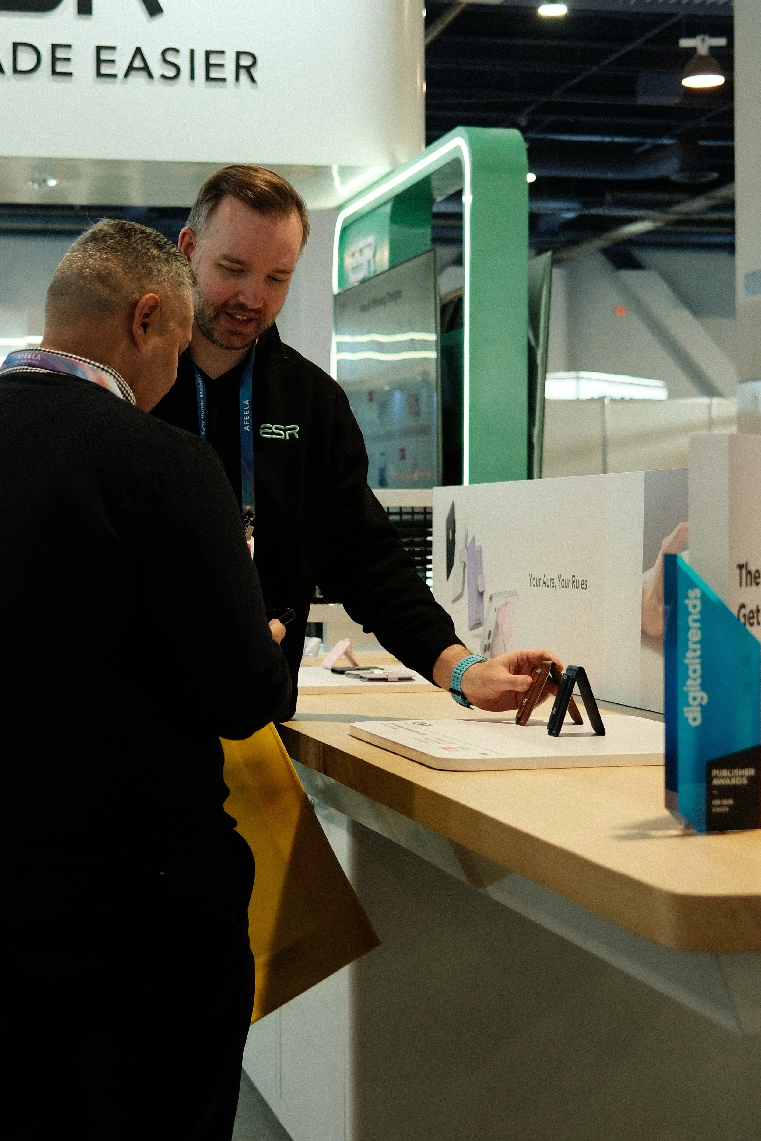 Two men at an exhibition booth looking at electronic devices on display.