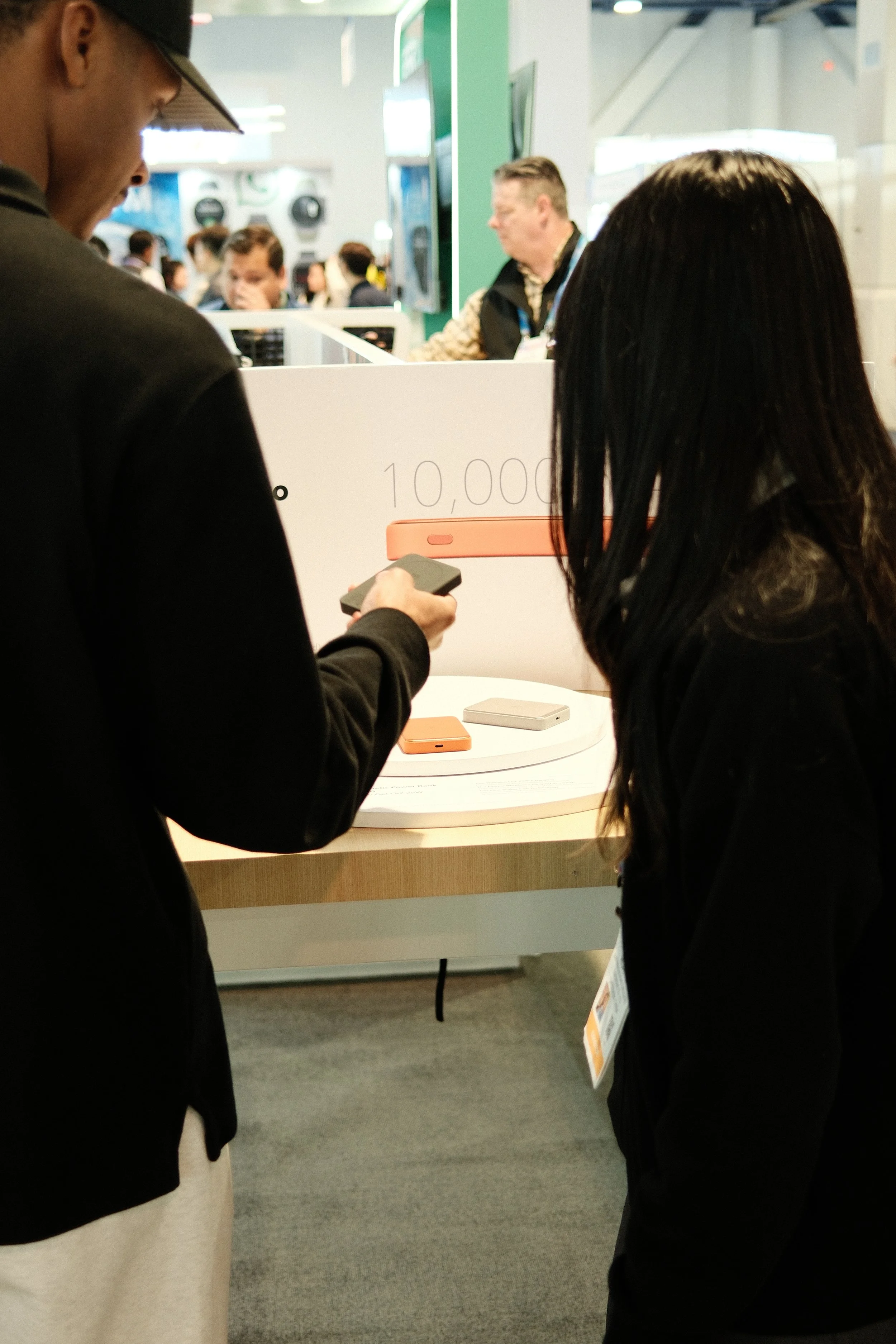 A man and a woman at a store display, with the man using his phone and the woman looking at the display that shows a device and the text '10,000' in the background.