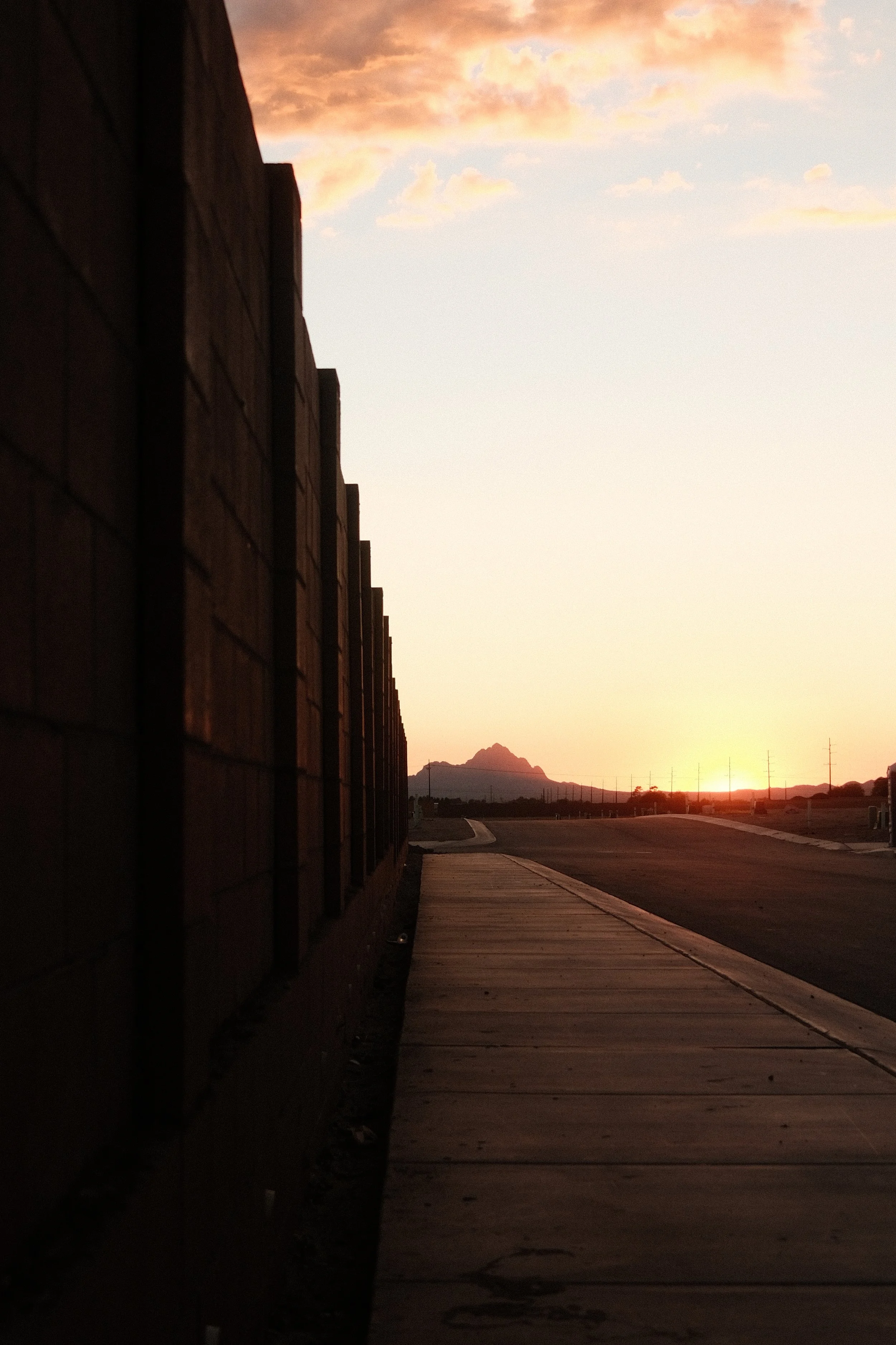 Sidewalk and brick wall at sunset with mountains in the distance and power lines.