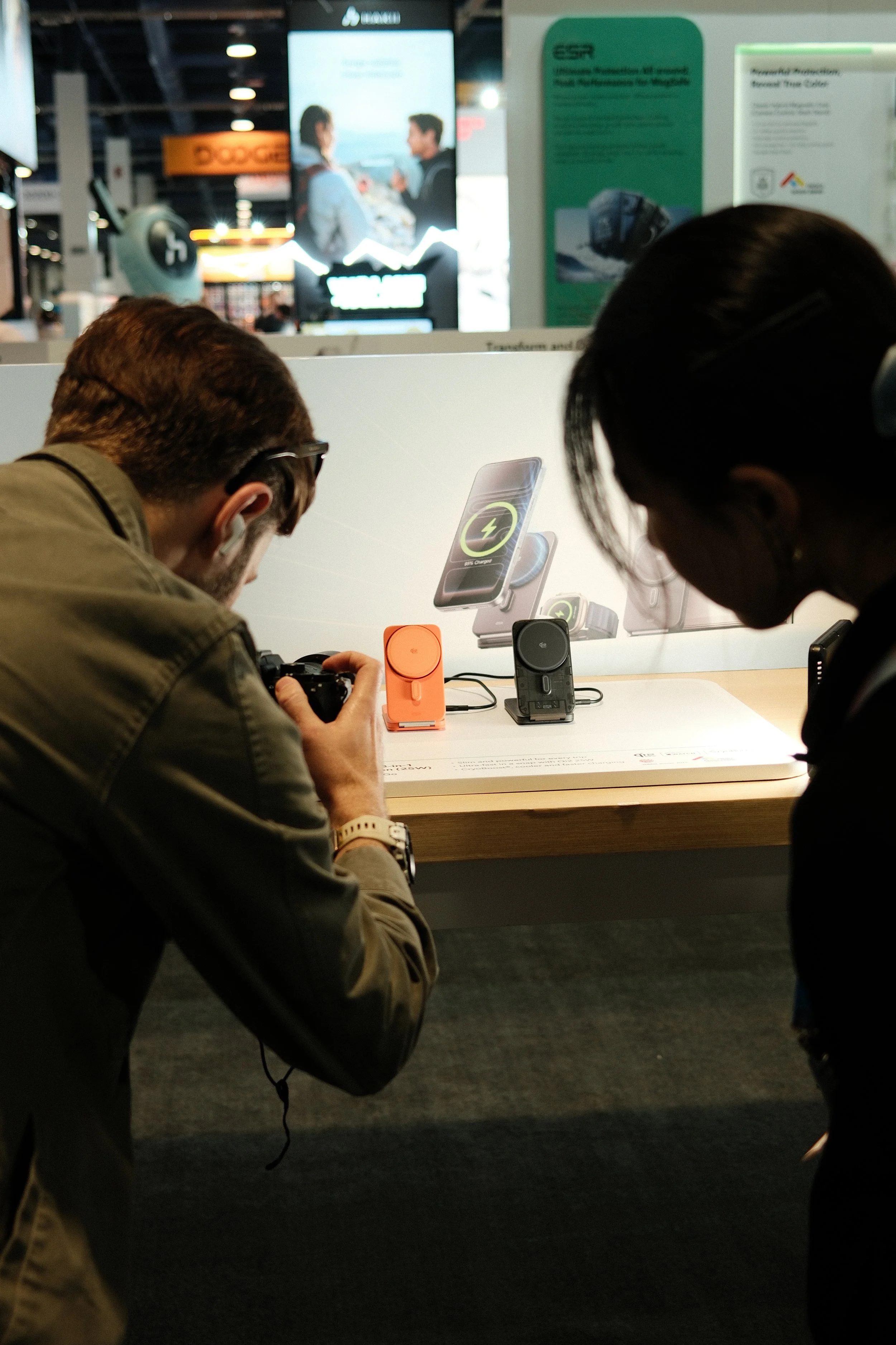 People examining wireless charging devices at an electronics store display with product images and informational posters in the background.