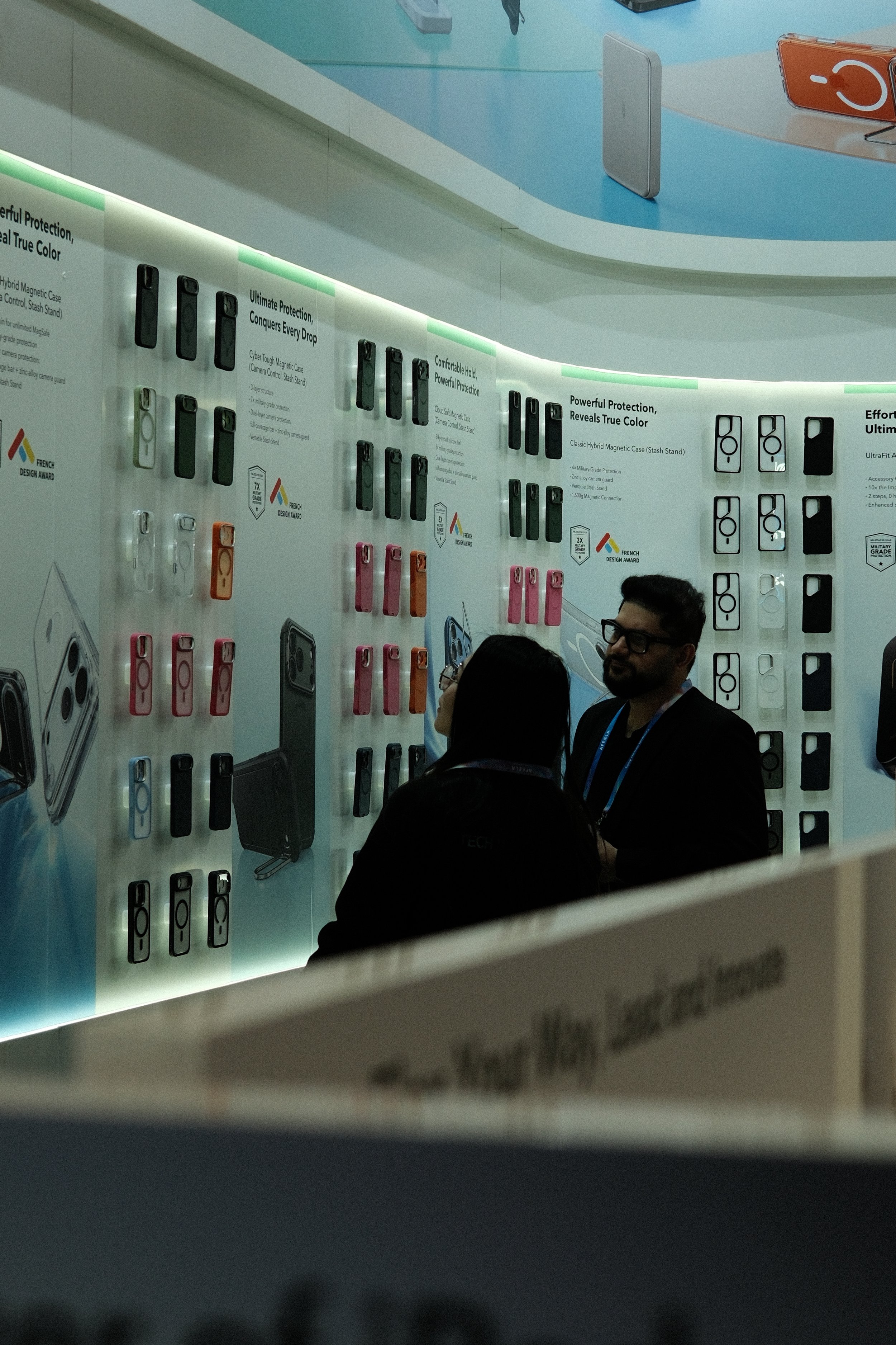 People looking at a display of various phone cases at a trade show or store.