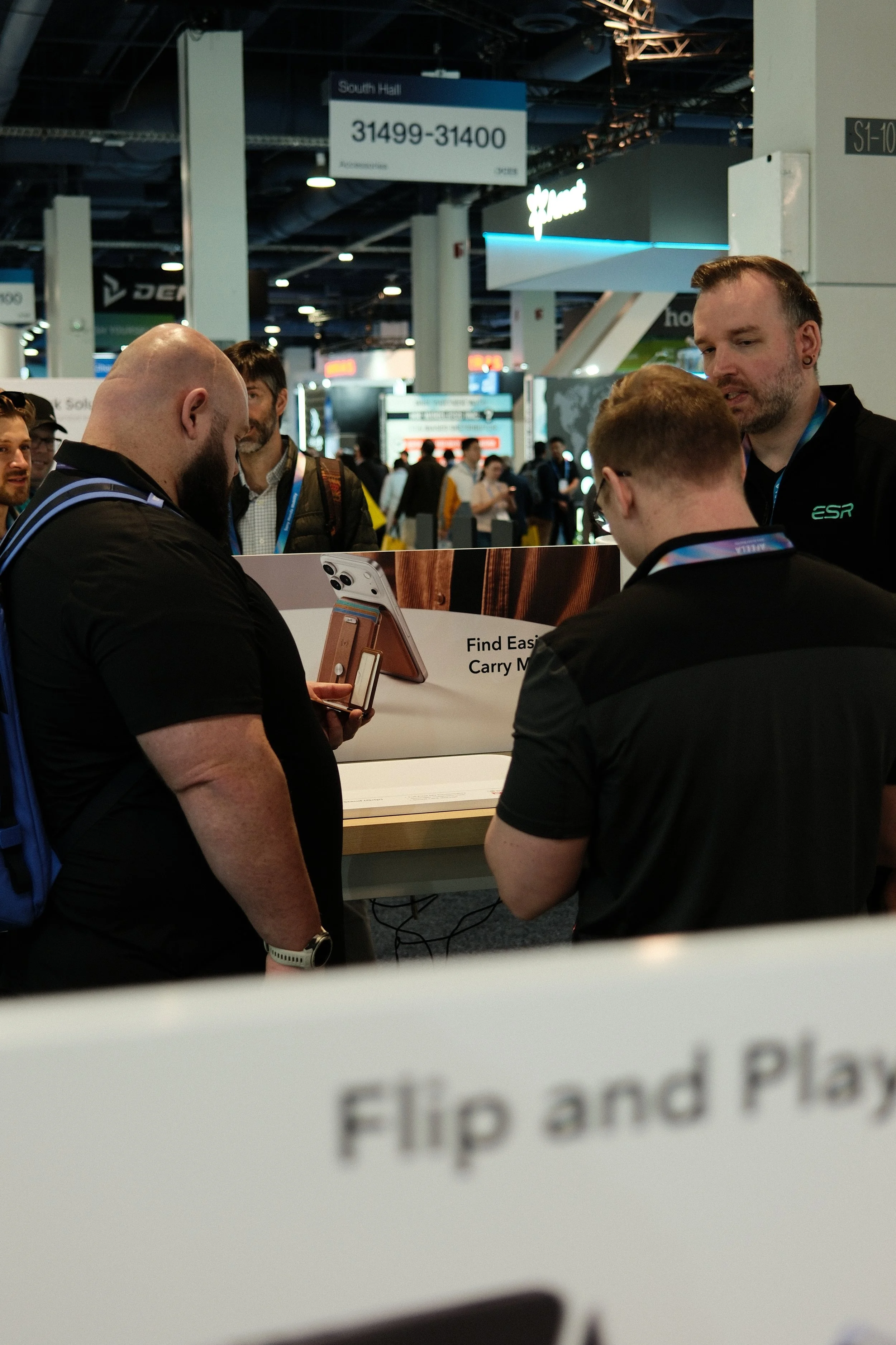 Group of people gathered around a display at a trade show or convention, with a sign that reads 'Find Easy Carry M...' and a partially visible sign below that says 'Flip and Play.'