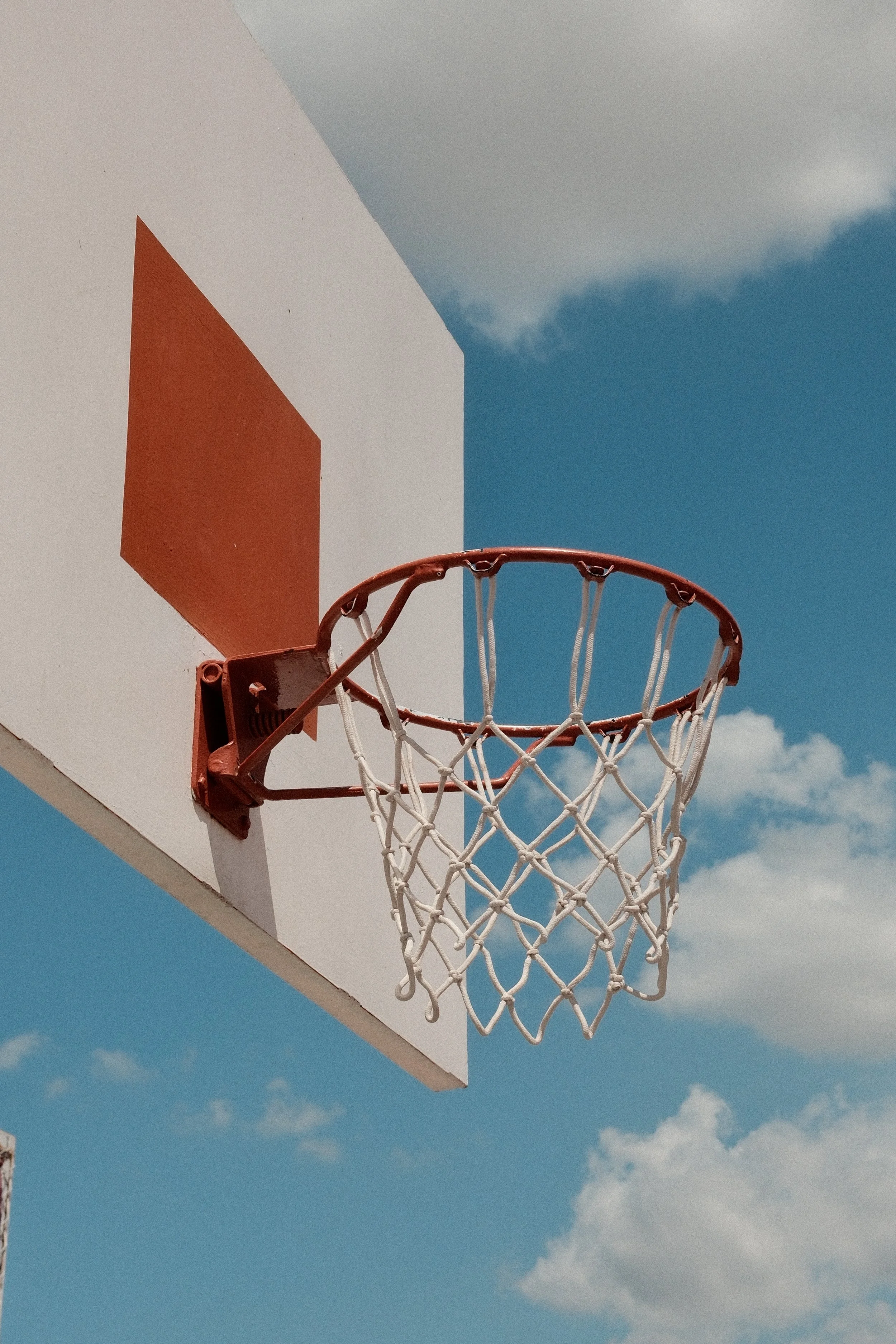 A basketball hoop mounted on a white backboard with a blue sky and clouds in the background.