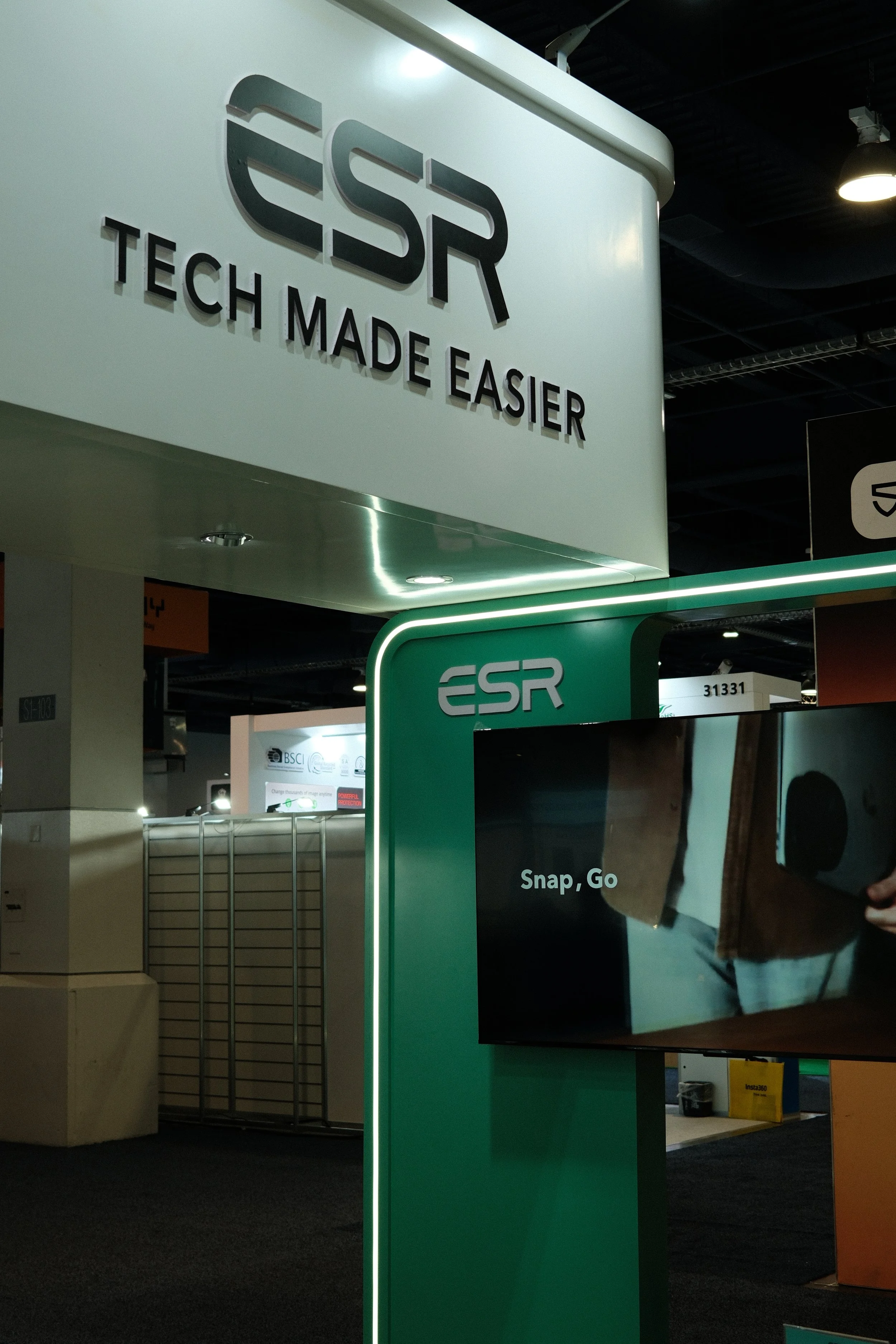 Trade show booth with the logo and slogan 'ESR - Tech Made Easier' on a large white sign. A green display with the ESR logo and the words 'Snap, Go' is in front of the booth.