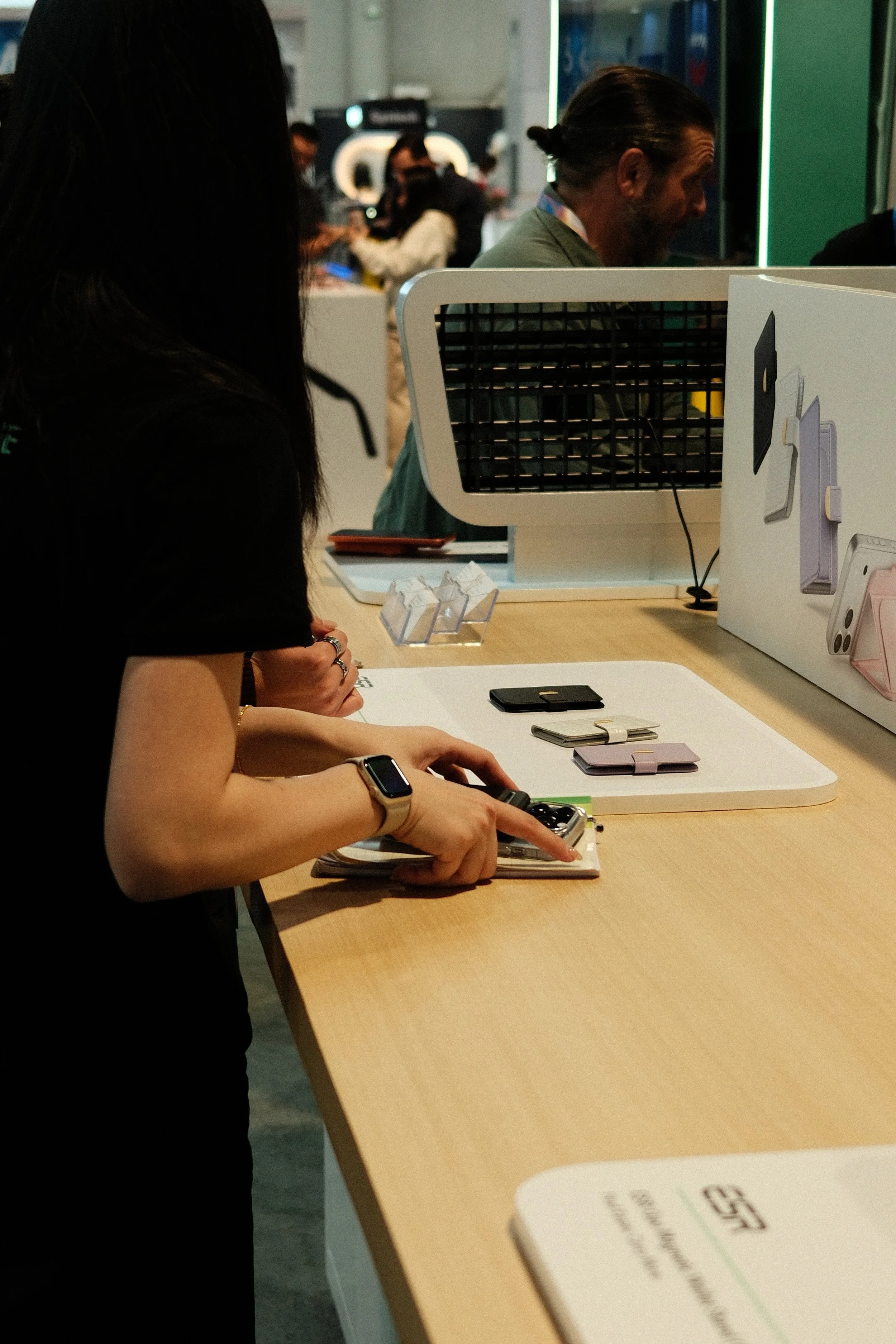A person with a smartwatch on their wrist shopping for tech accessories at a retail store, with various phone cases displayed on the table.