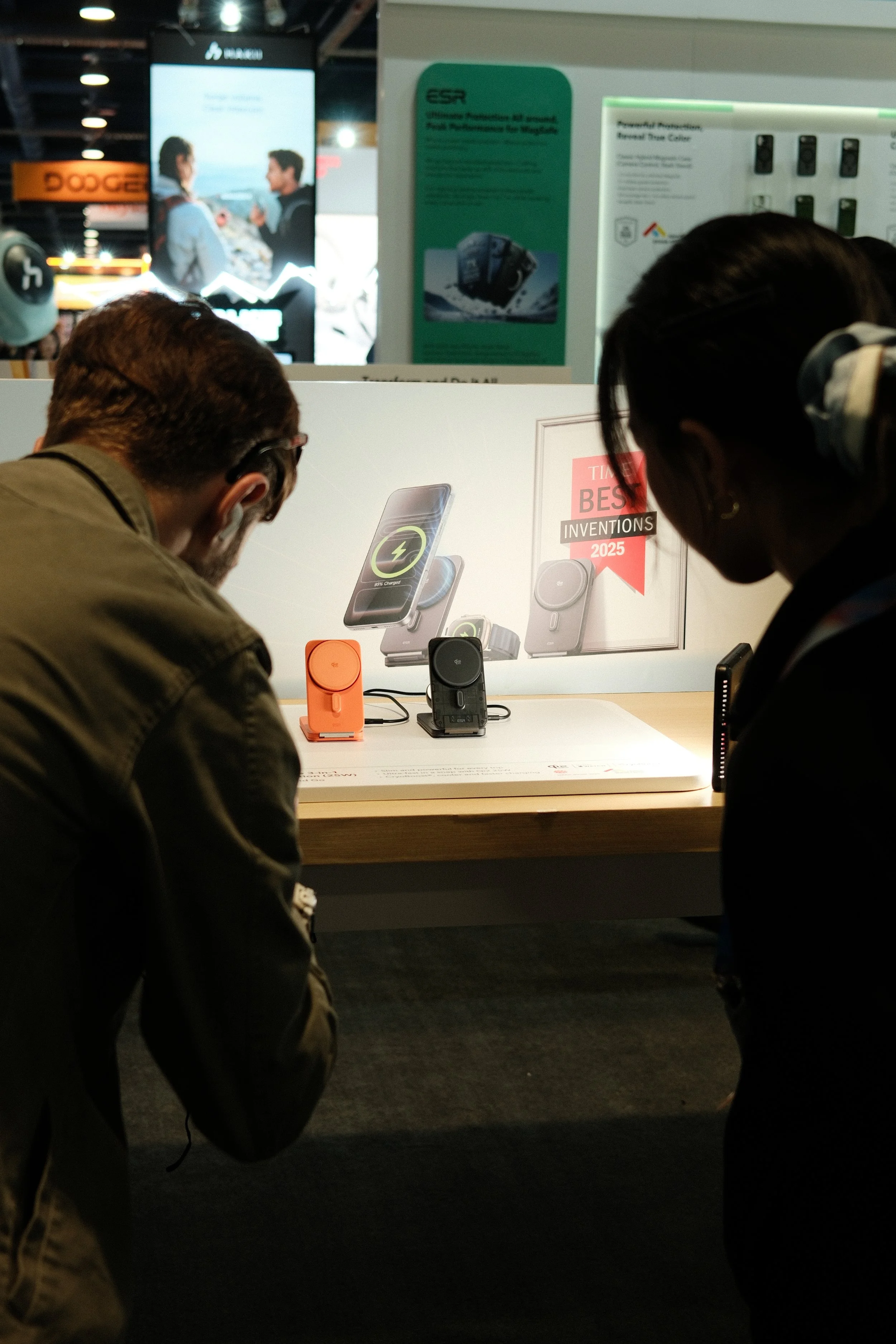 Two people looking at a display of wireless chargers on a store table, with promotional posters in the background.