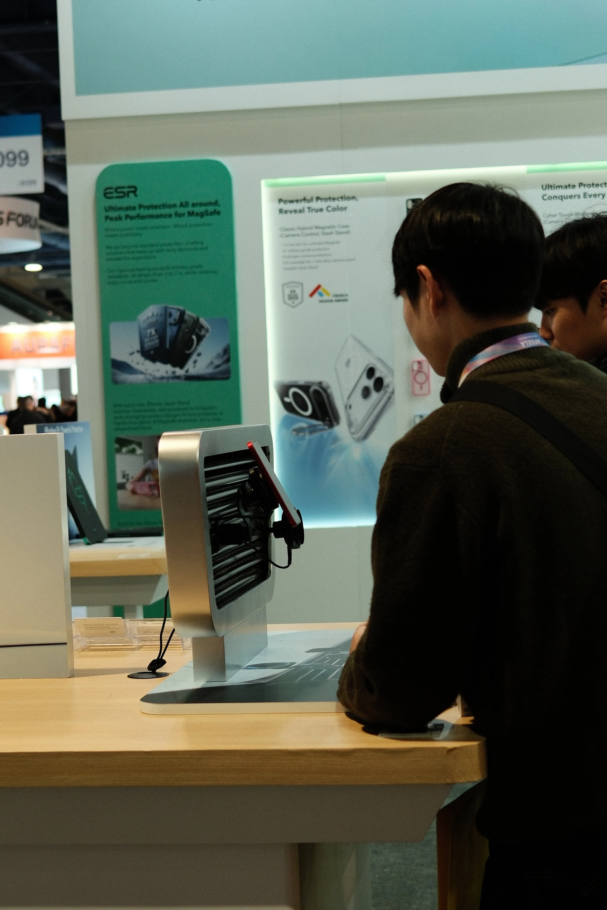 Man demonstrating a product at a trade show booth, with posters of camera lenses and accessories on the background.