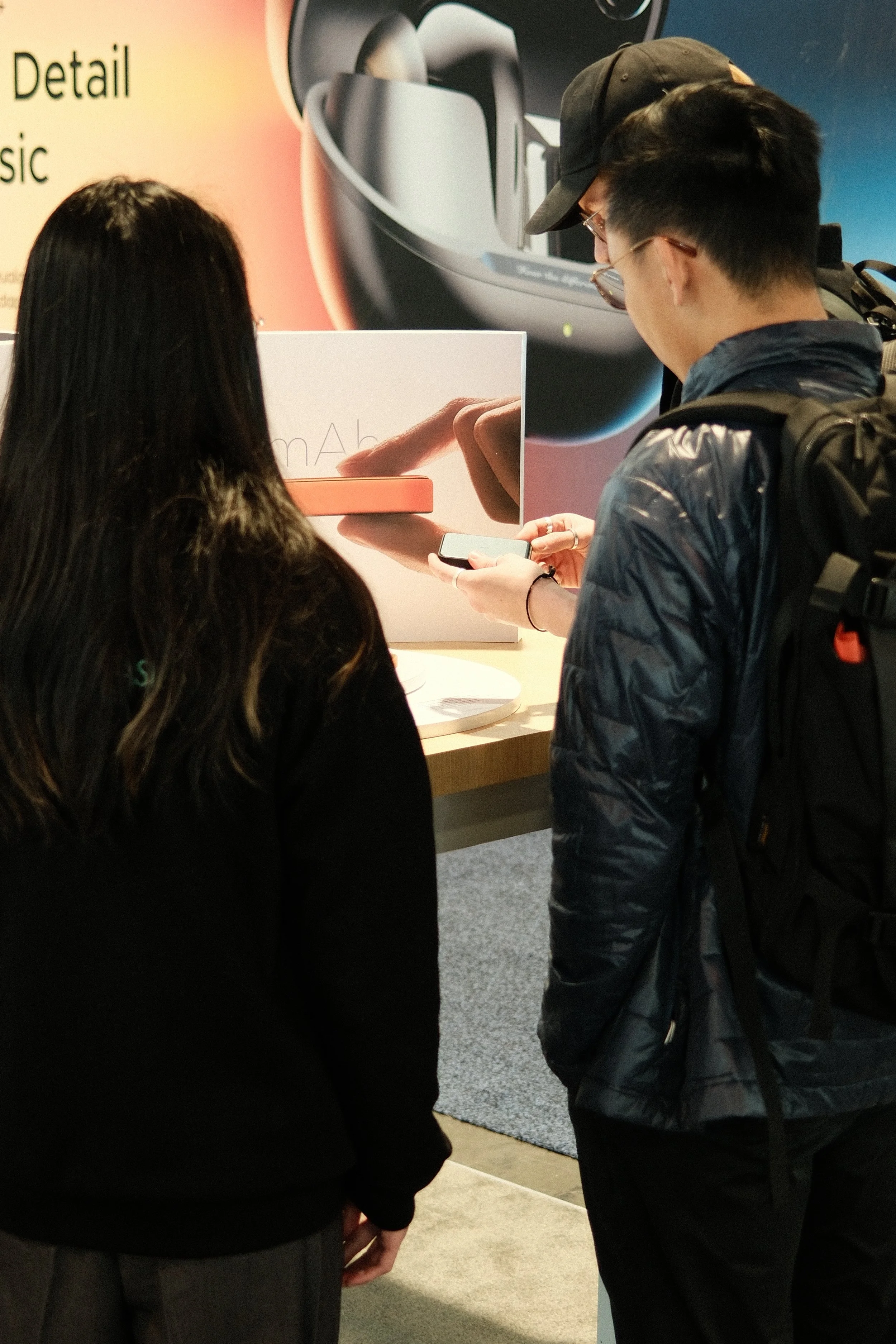 Two people standing at an Apple store display, looking at an iPhone and a promotional box for the iPhone.