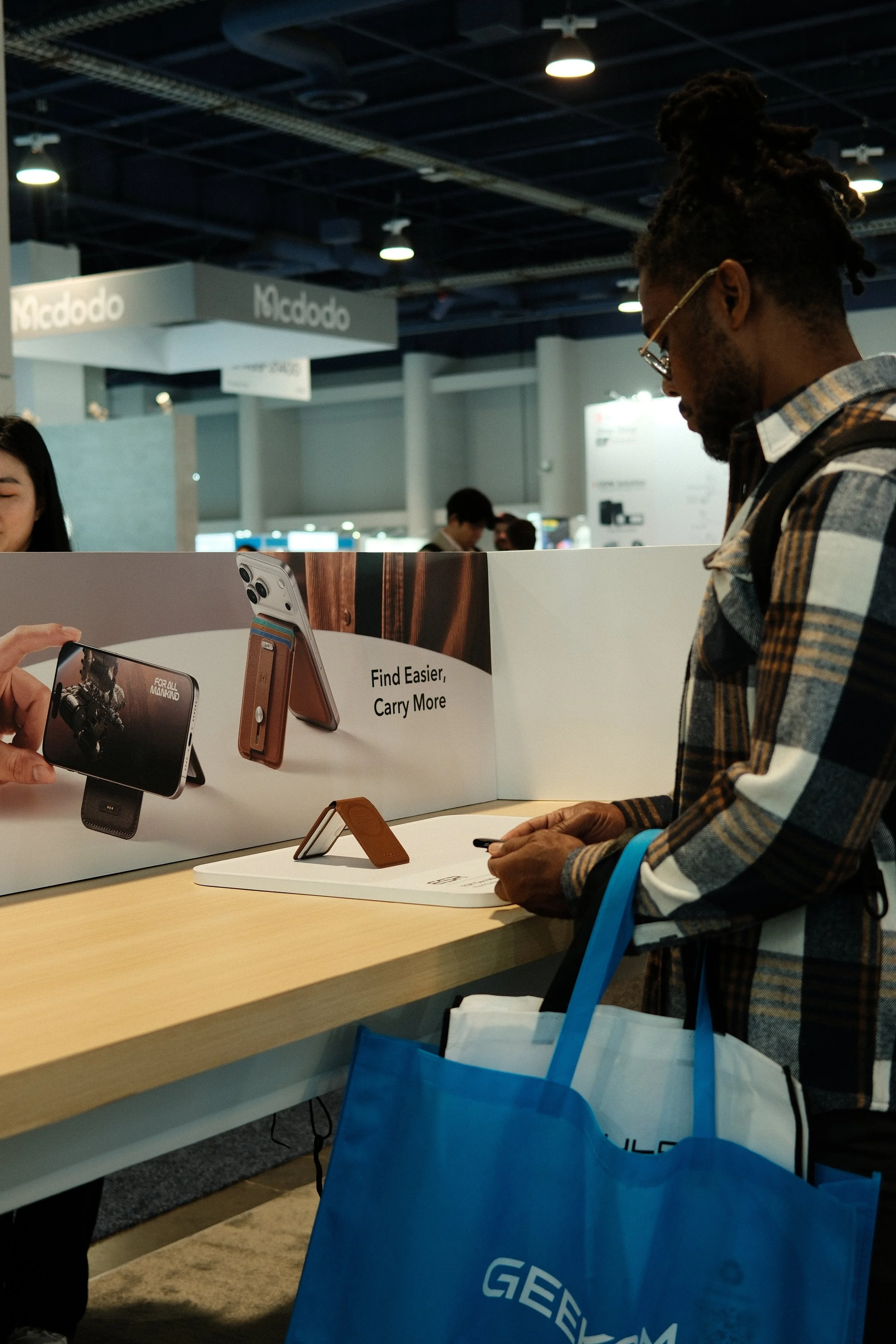 Man with glasses and a backpack looking at a display of mobile phone accessories in a retail store or exhibition.