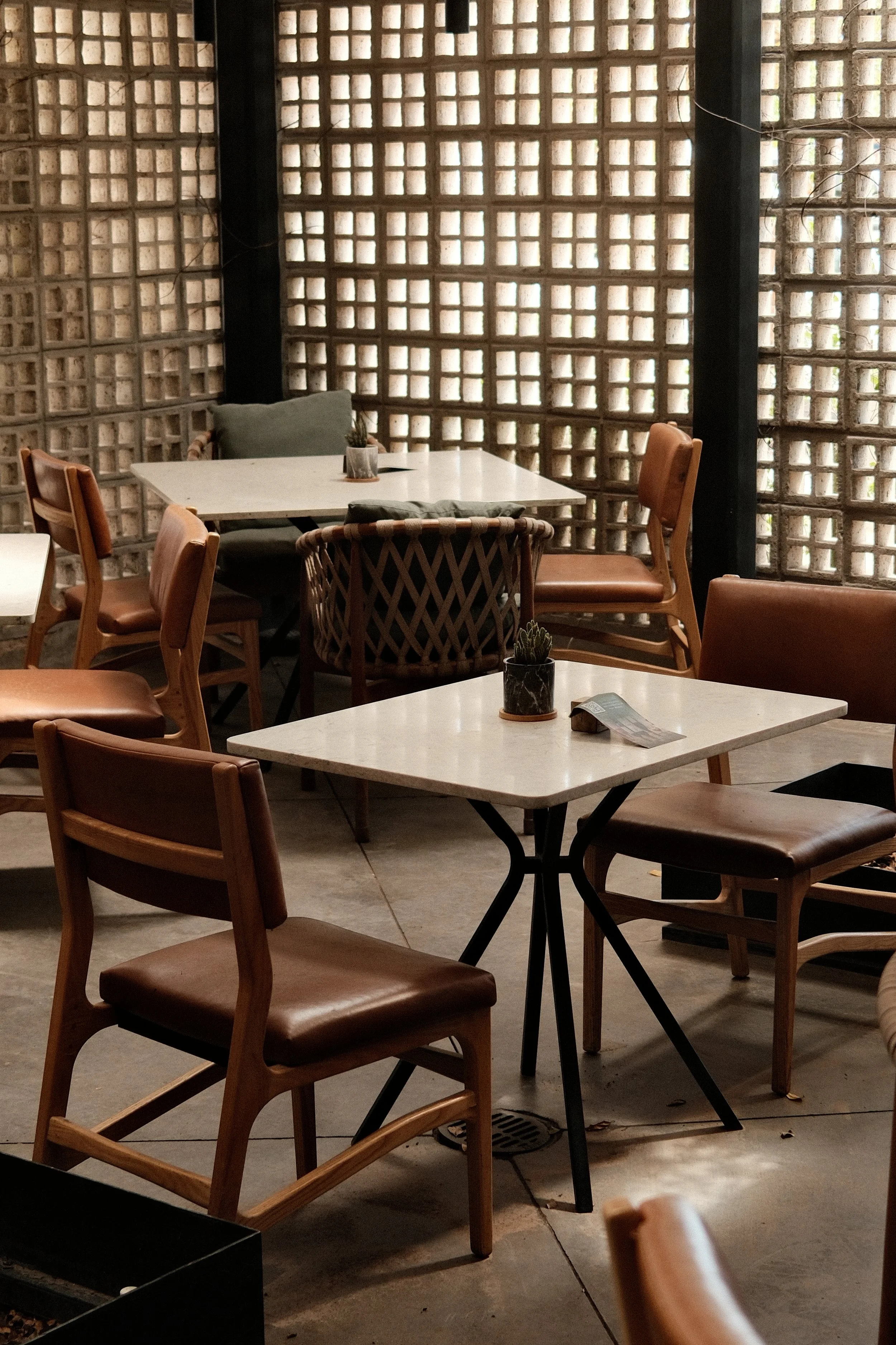 Indoor seating area with white marble tables, wooden chairs with brown leather seats, and a decorative brick wall in the background.