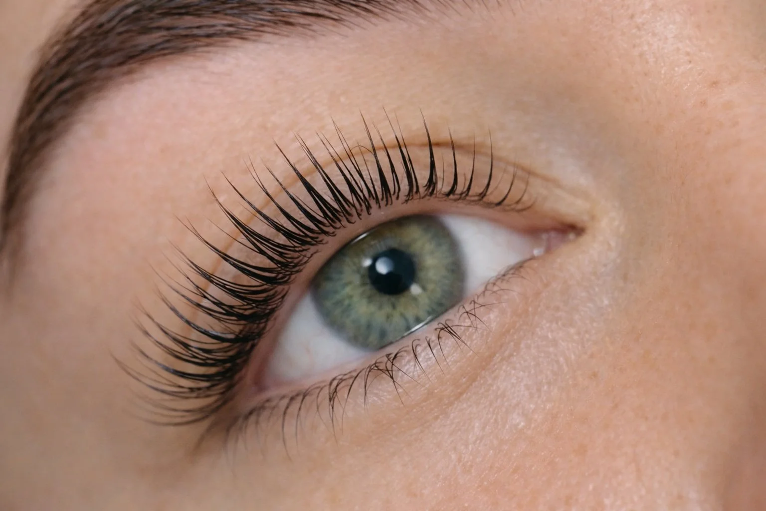 Close-up of a human eye with green iris and long black eyelashes.