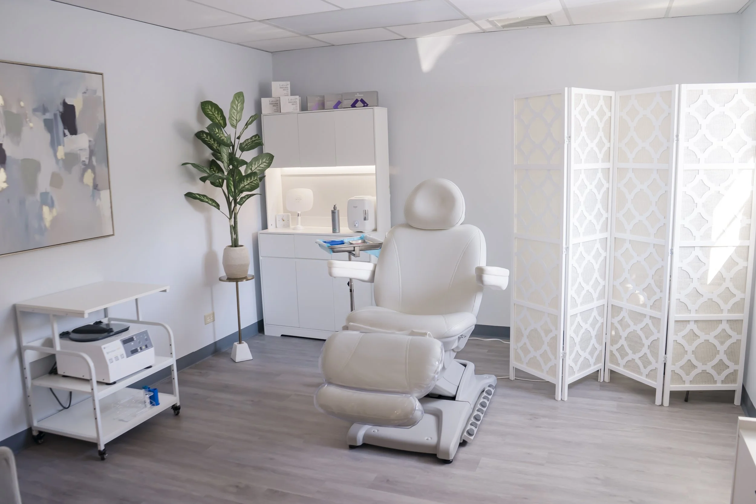 Medical treatment room with white medical chair, care supplies, and a light partition.