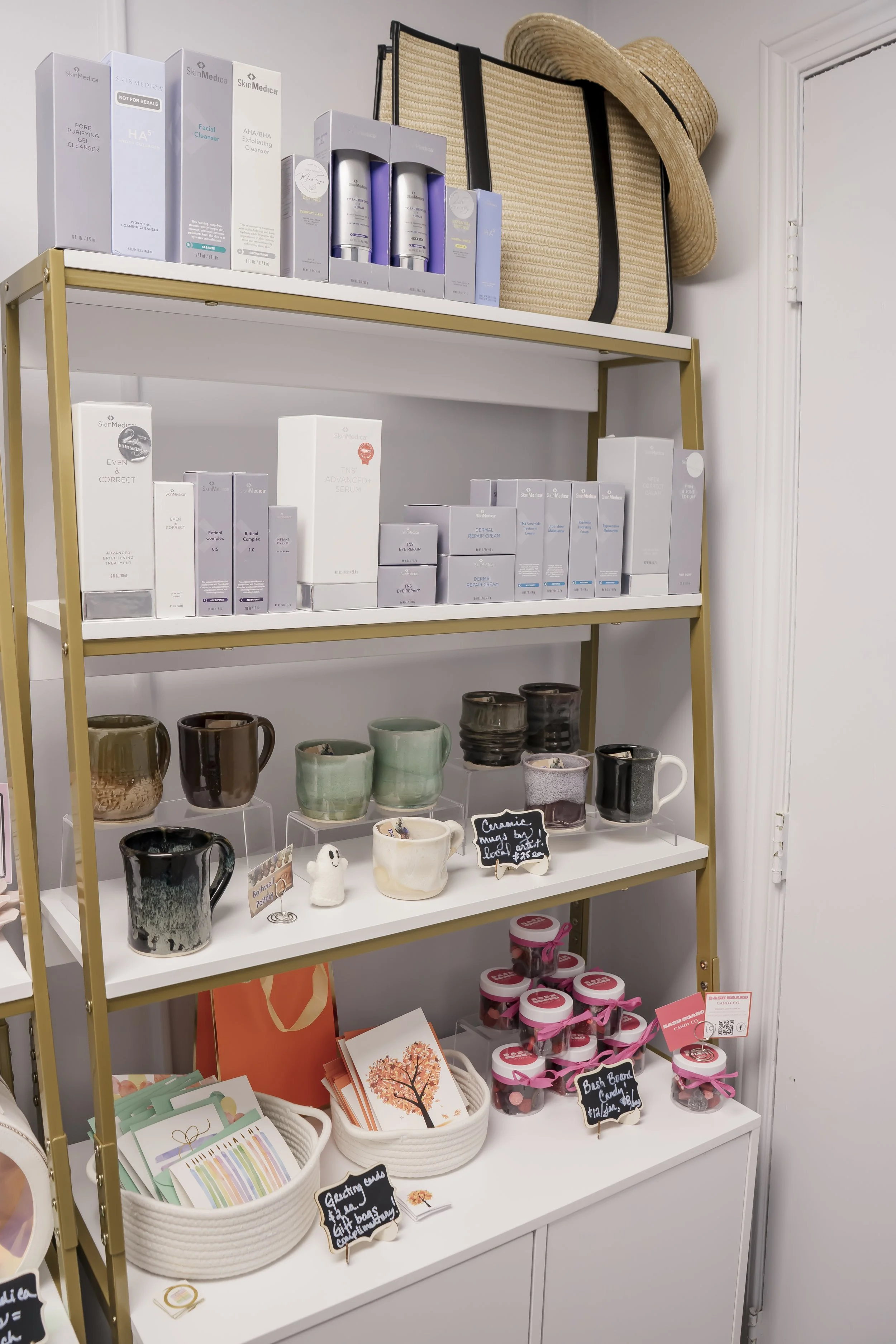 Retail shelf at Carla Thomas Med Spa displaying SkinMedica skincare products, handmade ceramic mugs, gift cards, and branded candy jars, styled with a mix of wellness and artisan gift items.