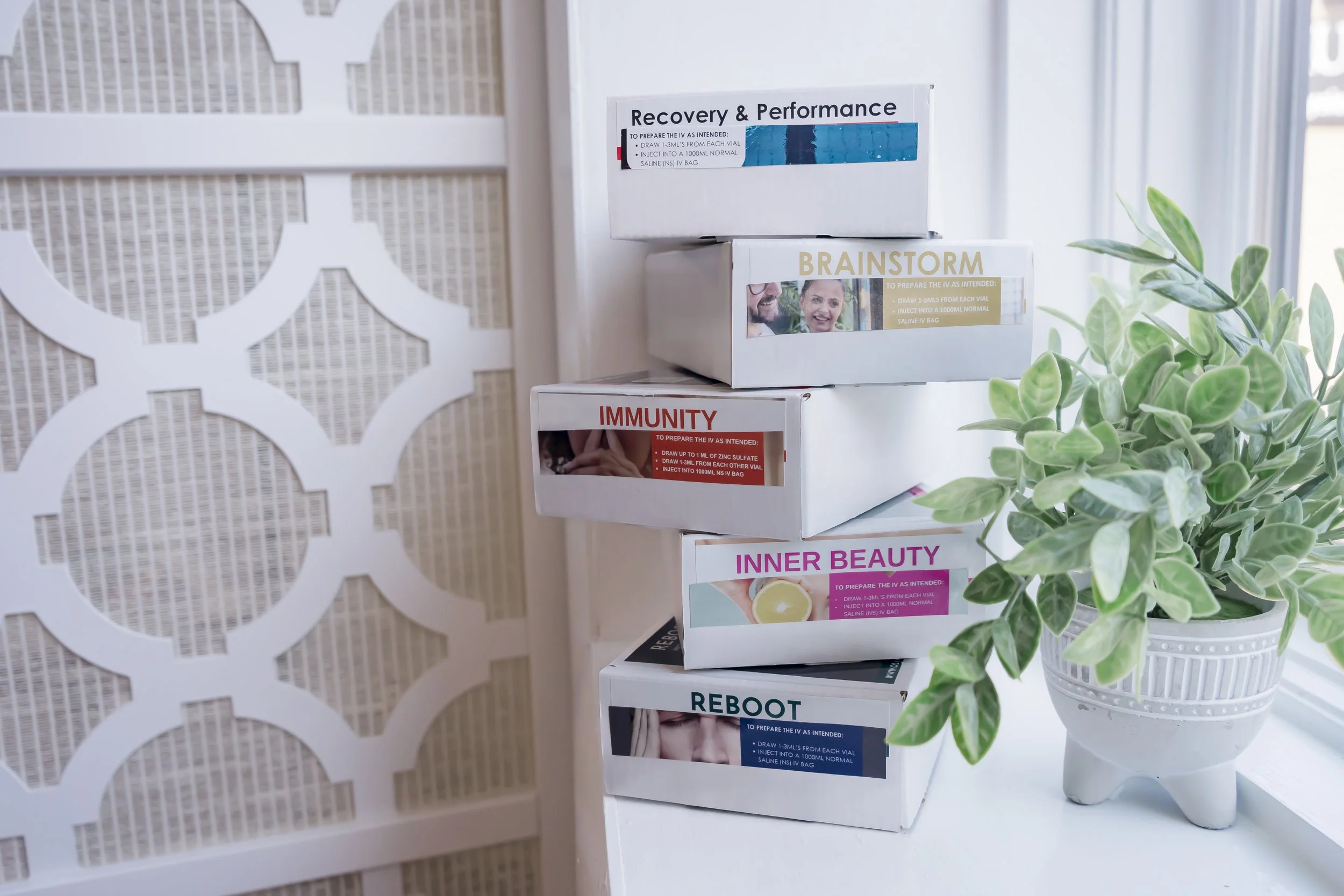 IV therapy kits labeled Reboot, Immunity, Inner Beauty, Brainstorm, and Recovery & Performance stacked beside a plant at Carla Thomas Med Spa.