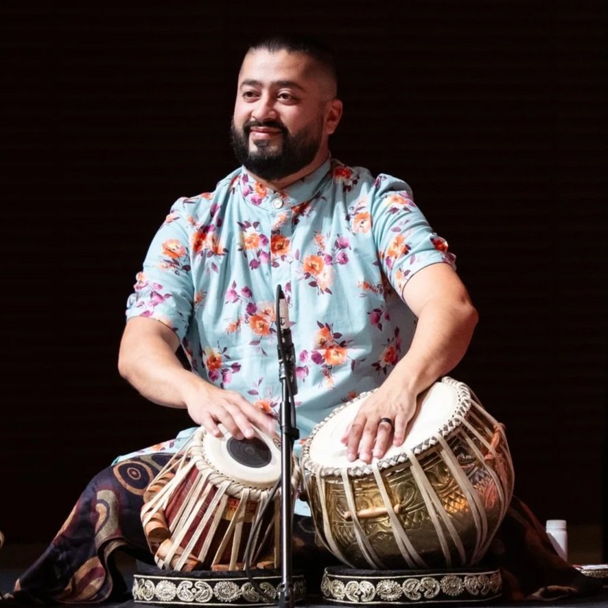 Vinay Sharma aka Vin Rocc playing tabla drums on stage, wearing a floral kurta and seated on stage at the Festival of Tabla, with a microphone nearby.