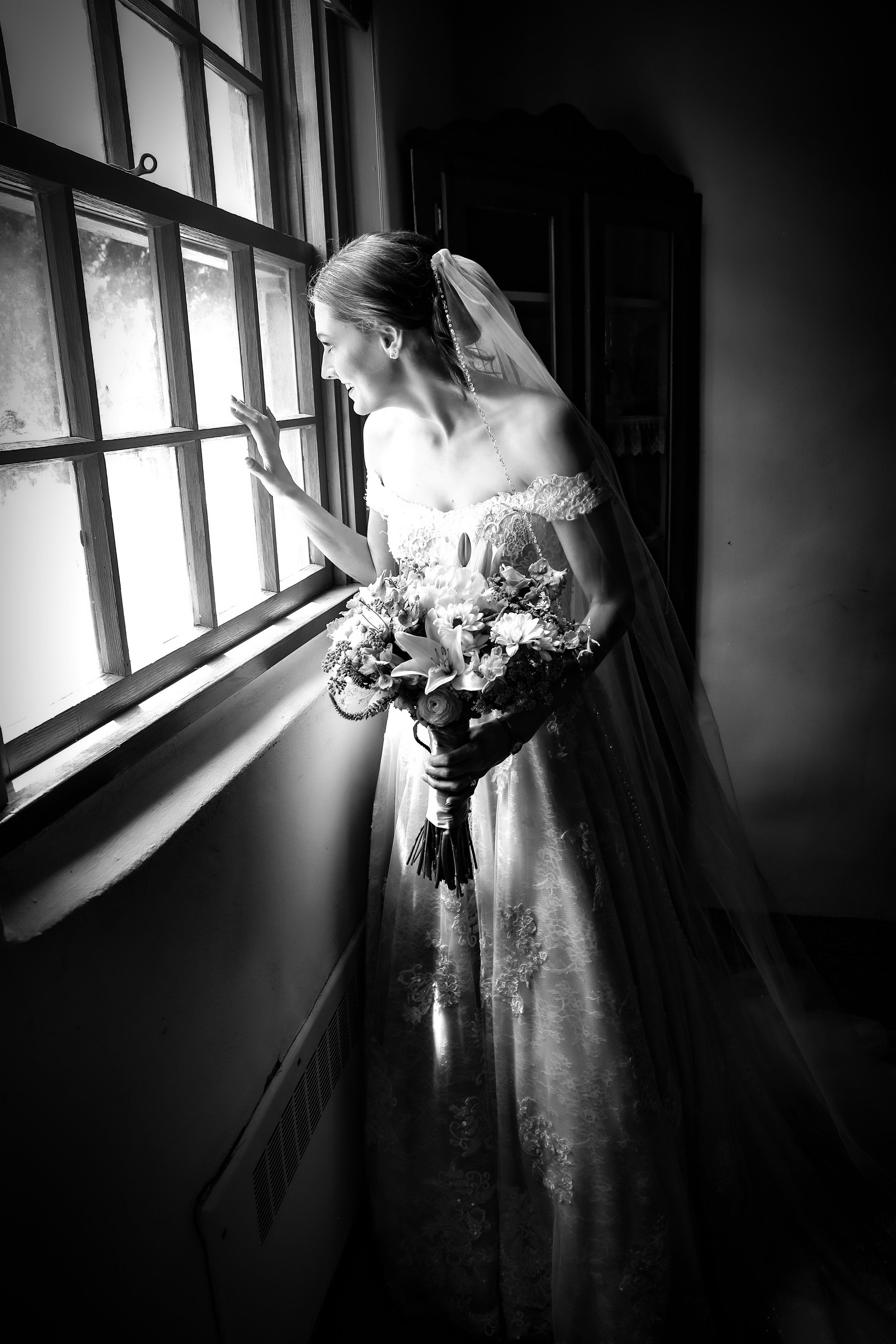Black and white image of Bride looking out the window  before her wedding