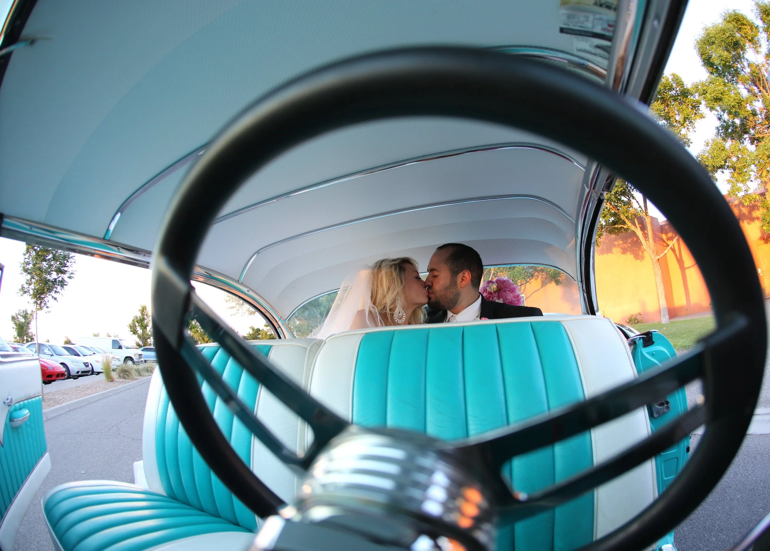 Couple photographed kissing through the steering wheel of classic car.JPG