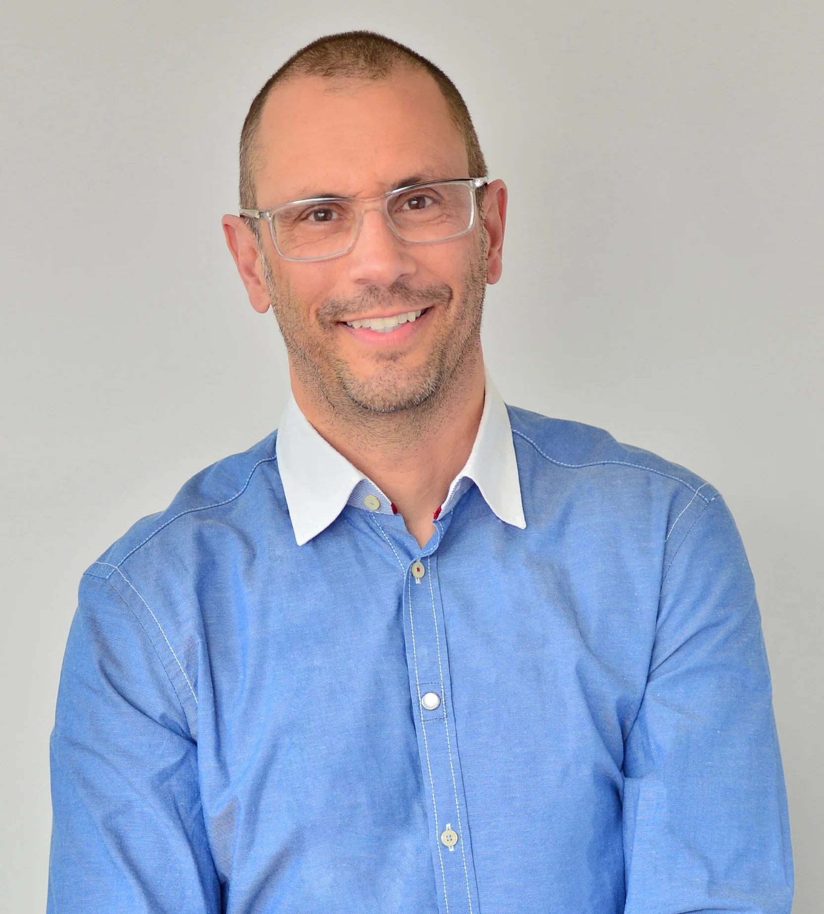 Un homme souriant portant des lunettes et une chemise bleue.