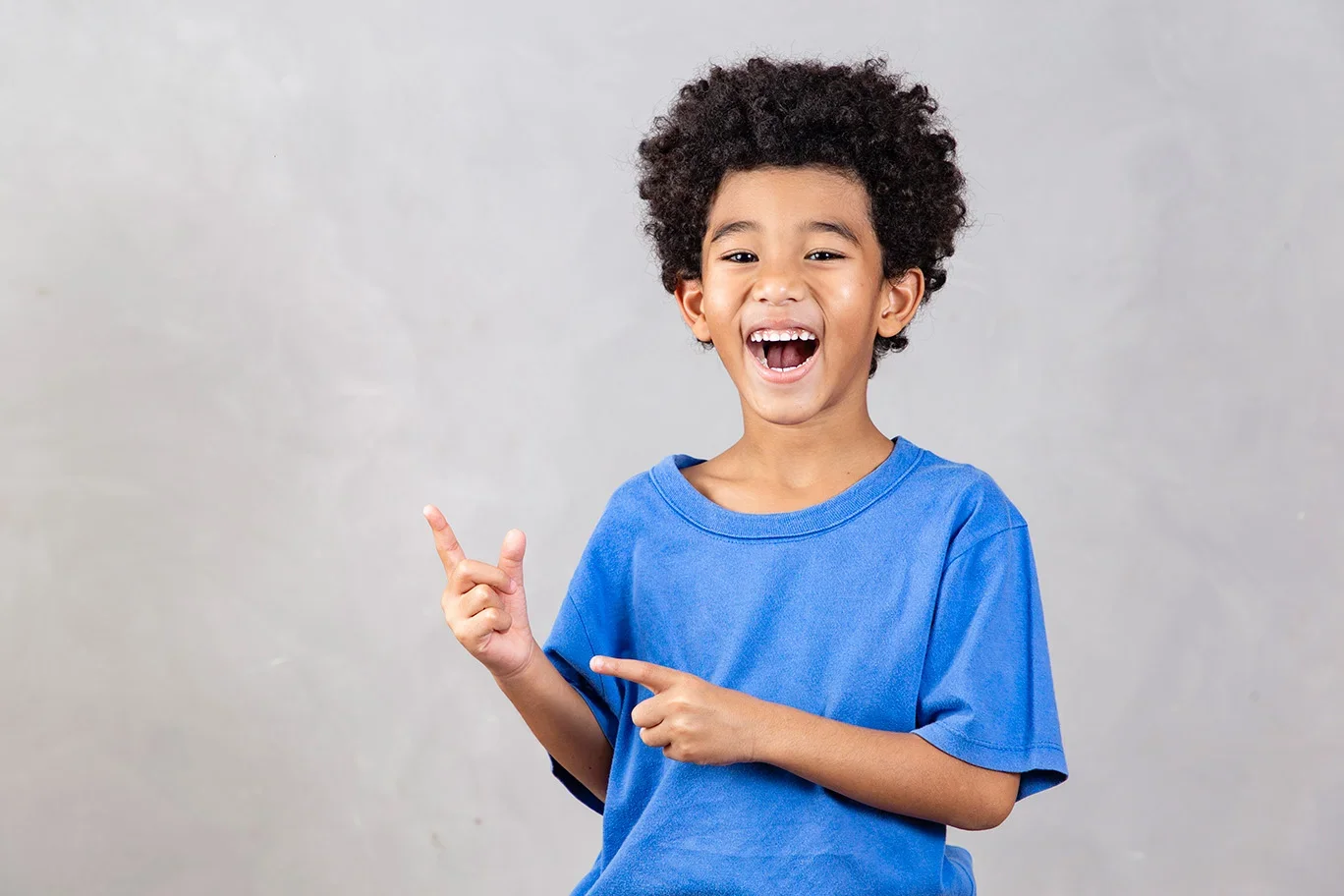Un garçon souriant portant un t-shirt bleu, pointant du doigt tout en étant heureux.