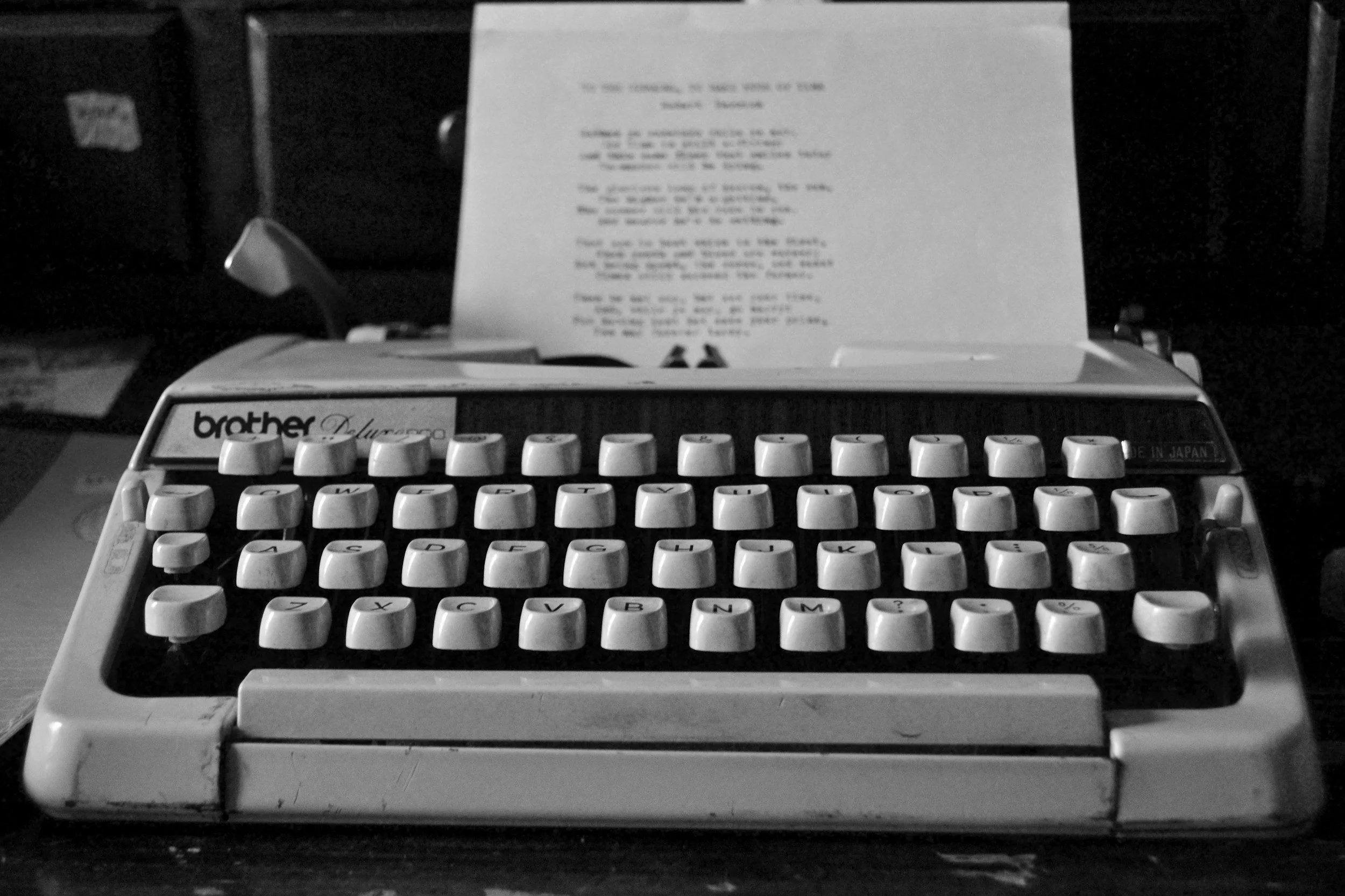 A vintage typewriter with a sheet of paper inserted, placed on a dark surface. The typewriter is a Brother Deluxe 2000 model, with keys visible in the foreground.