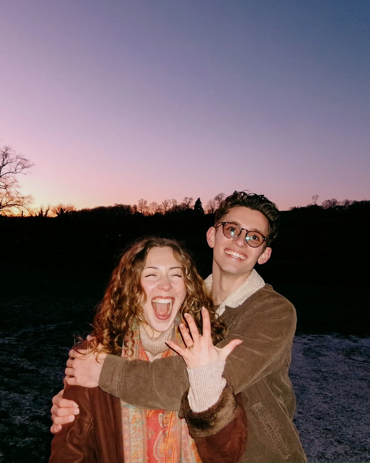 Happy young couple hugging outdoors during sunset on a dark water body background.