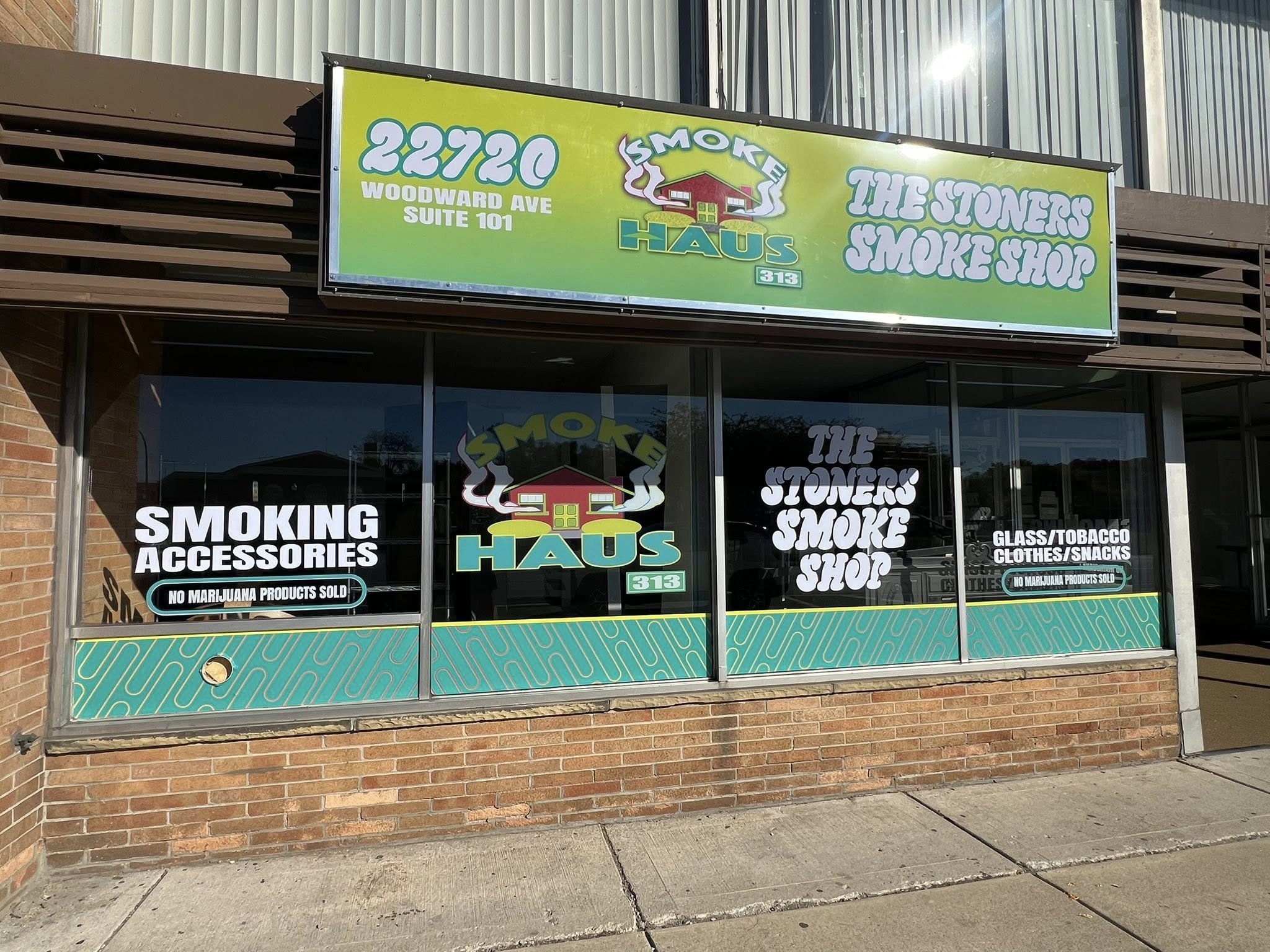 Storefront signage for The Stones Smoke Shop and Smoke Haus, located at 22720 Woodward Ave, Suite 101, with signs indicating the shop sells smoking accessories, glass, tobacco, clothes, snacks, and that no marijuana products are sold.