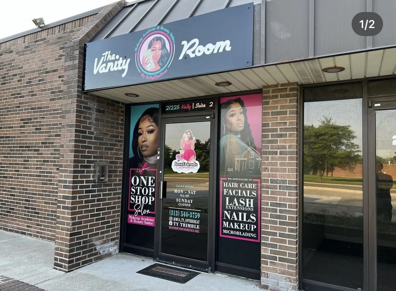 The exterior of a beauty salon named The Vanity Room with large promotional posters of women with styled hair, nails, and makeup. The signage indicates services like hair care, facials, lash extensions, nails, makeup, and microblading.