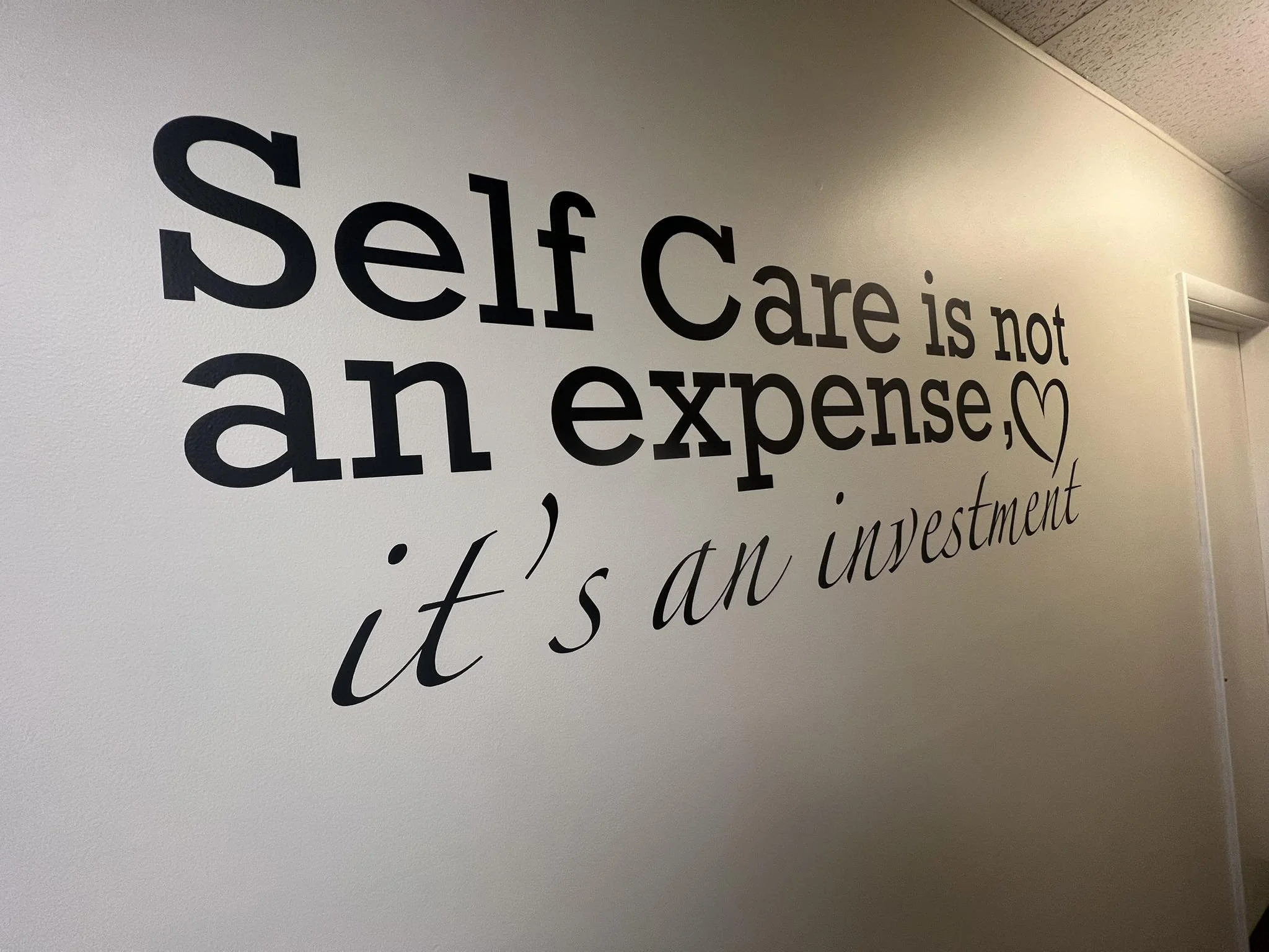 Wall quote that reads 'Self Care is not an expense, it's an investment' with a heart symbol.