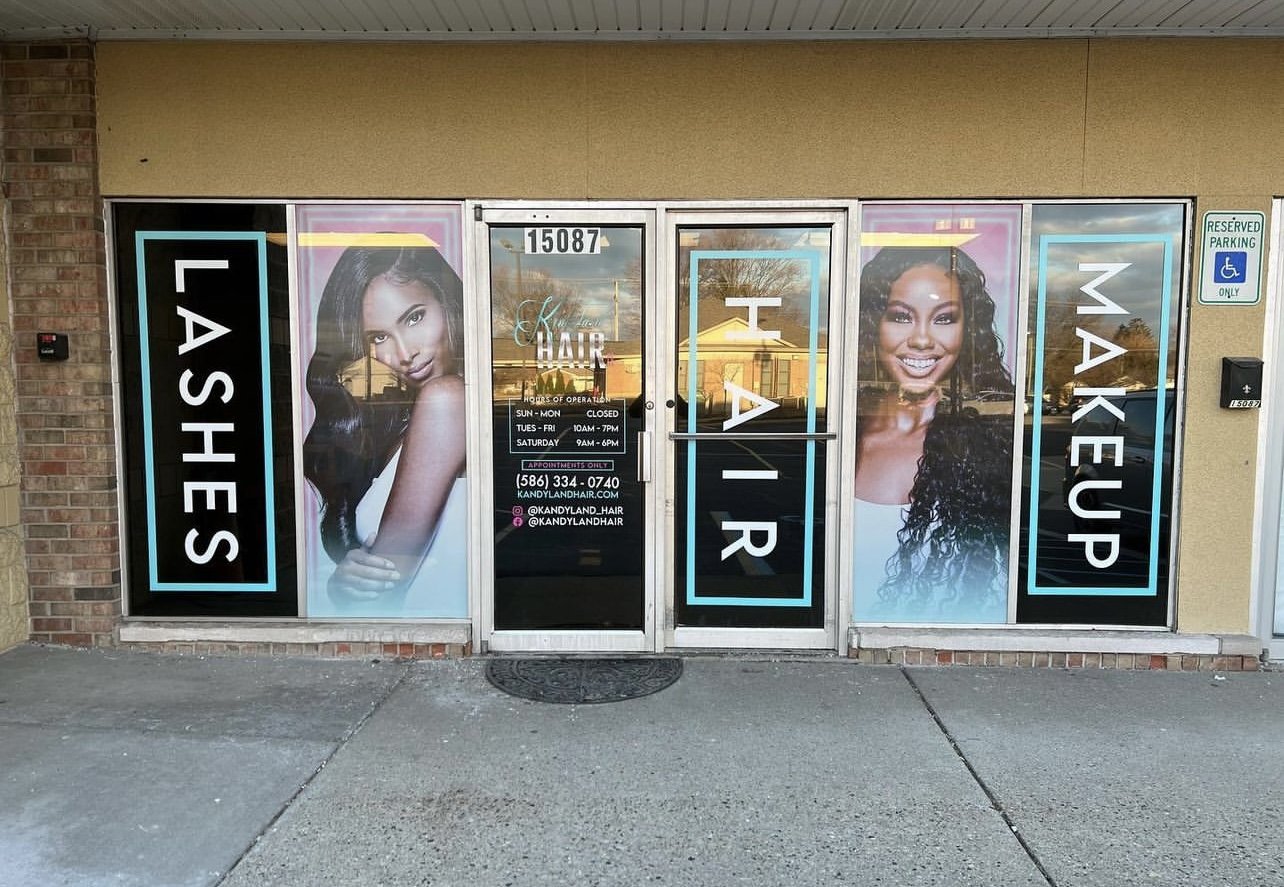 Front of a hair salon with large posters of women with different hairstyles and the words "LA SHE S HAI R MAKE UP" displayed on the windows.