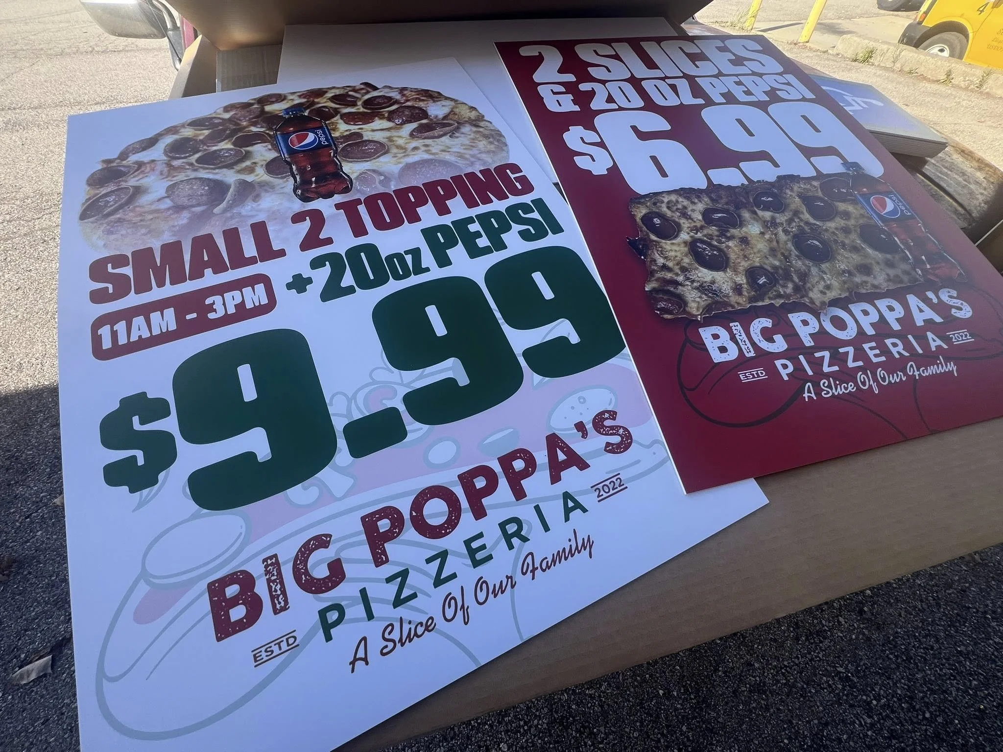 Promotional posters for Big Poppa's pizzeria advertising special pizza deals; one poster features a large pepperoni pizza with a small 20 oz Pepsi and is priced at $9.99, available from 11 am to 3 pm; the other poster displays a different pizza with 