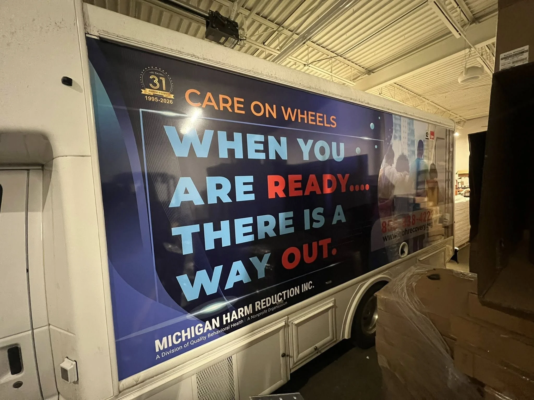 A large advertisement truck with a blue background, highlighting the 31st anniversary of Michigan Harm Reduction Inc., featuring a message about caring on wheels and a quote about being prepared to find a way out, with contact information and a websi