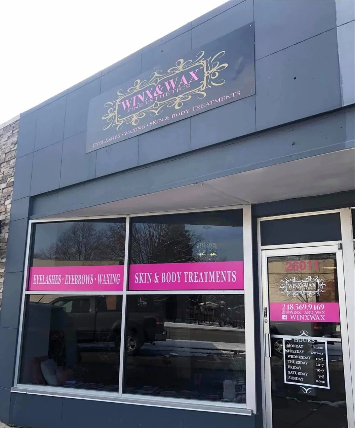 Exterior of a beauty salon with signage for eyelash, eyebrow, waxing, skin, and body treatments, featuring pink and black lettering.
