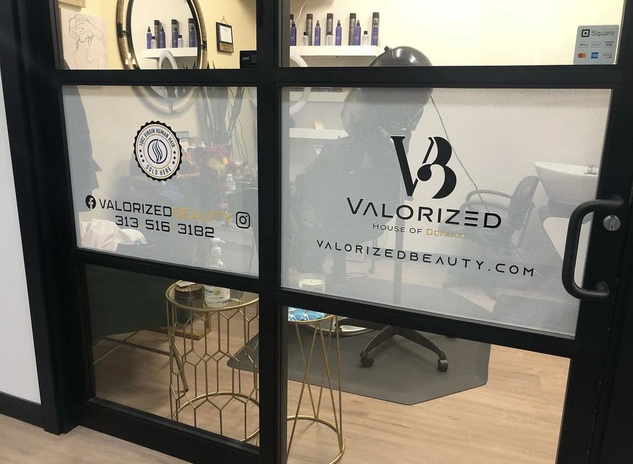 Glass door with Valorizad Beauty logo and contact information, revealing a beauty salon interior with treatment chair, shelves with bottles, and decorative wall art.
