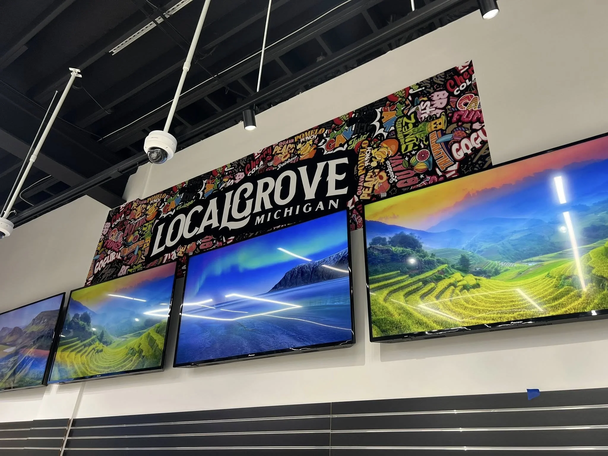 Sign reading 'Local Grove Michigan' above three digital screens displaying scenic landscape photos of Michigan's countryside