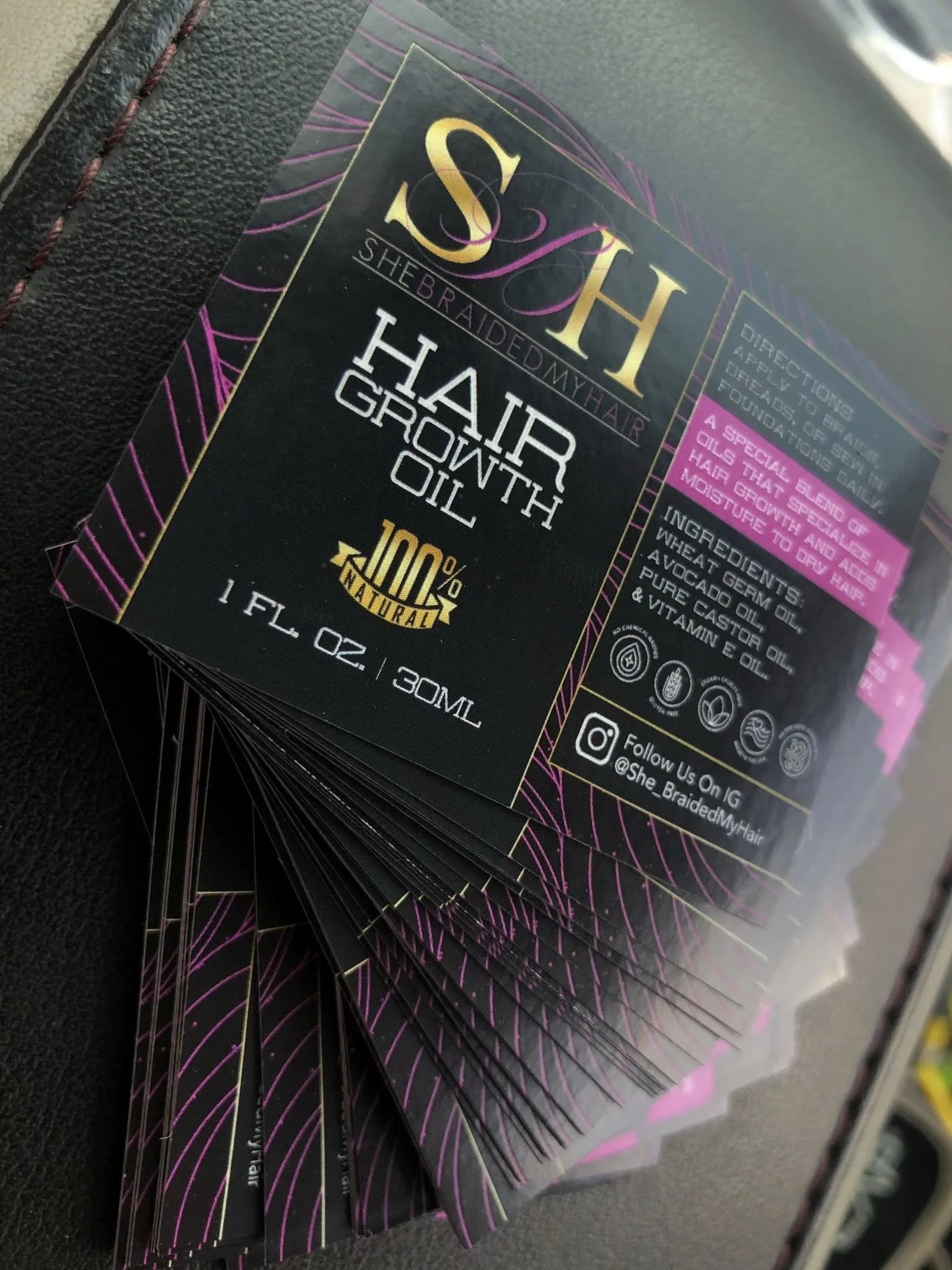 Stack of black hair growth oil bottles with purple and gold accents.