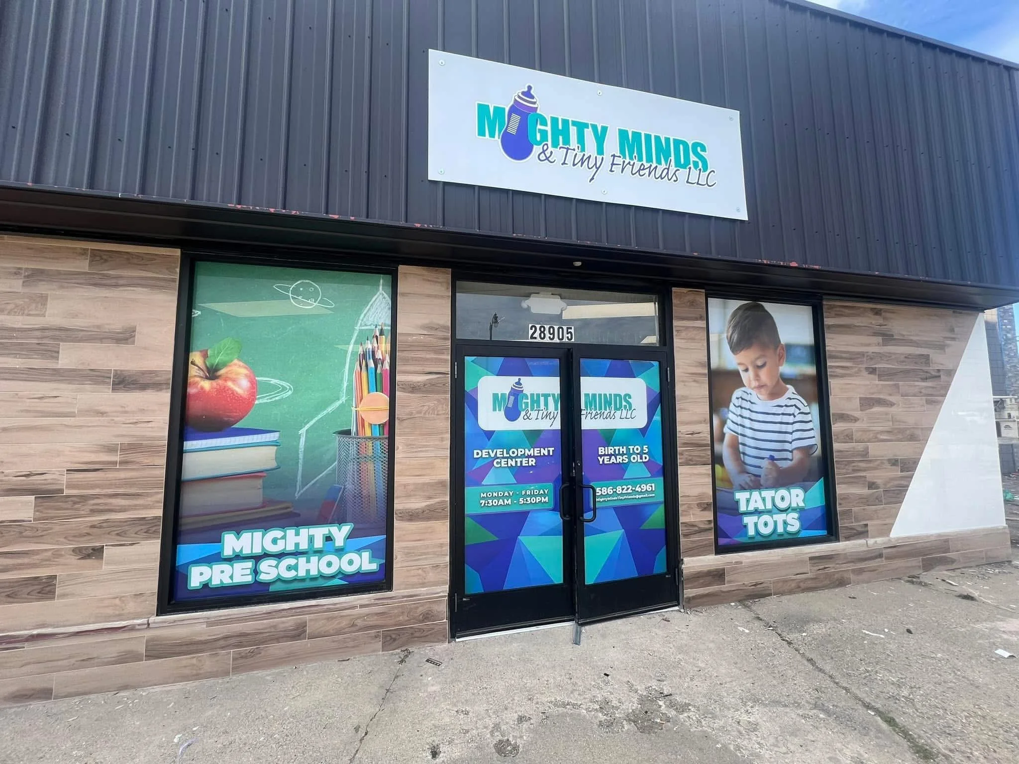 Exterior of a childcare center called Mighty Minds & Tiny Friends LLC, with signs indicating it as a development center for children from birth to 5 years old, featuring colorful graphics and a young boy.