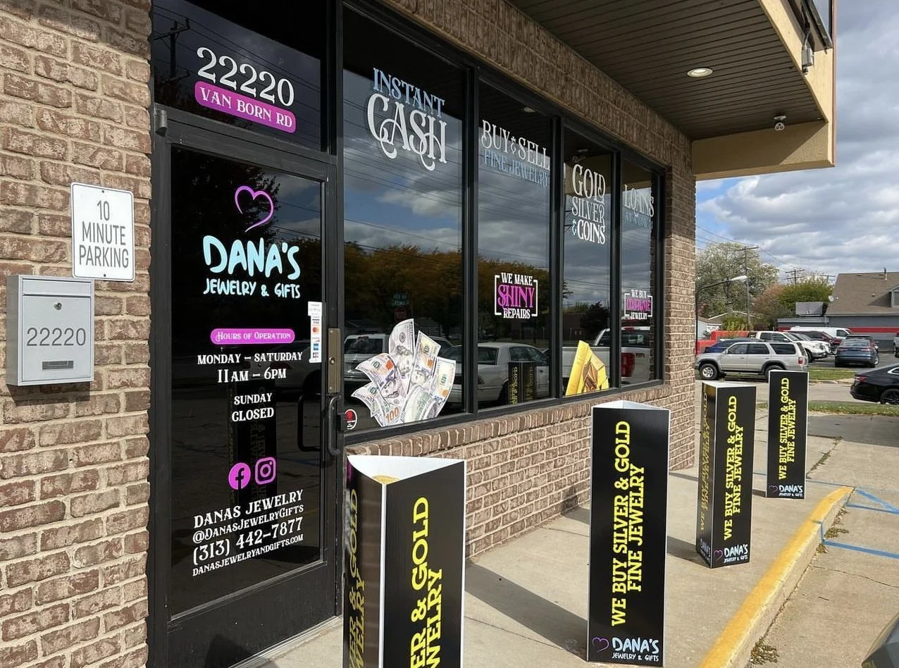 Front view of Dana's Jewelry & Gifts storefront with window signs advertising jewelry, gifts, gold, silver, coins, and services like cash buy and sell; two signs outside promote buying silver and gold, and parking instructions are visible.