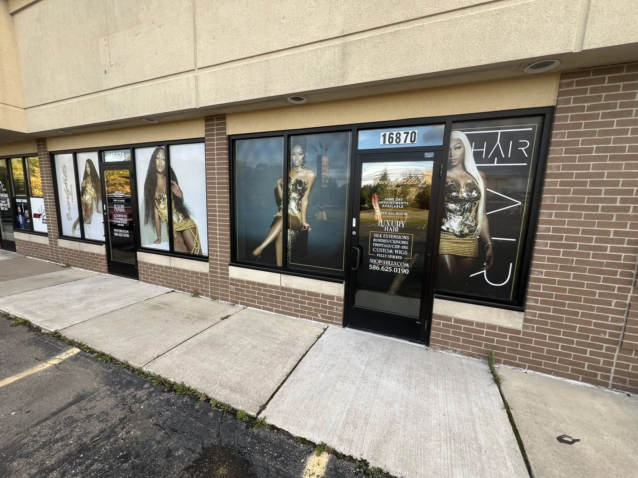 Shop storefront with large posters of women with long hair in gold and black outfits, advertising luxury hair products and services, including wigs and extensions.