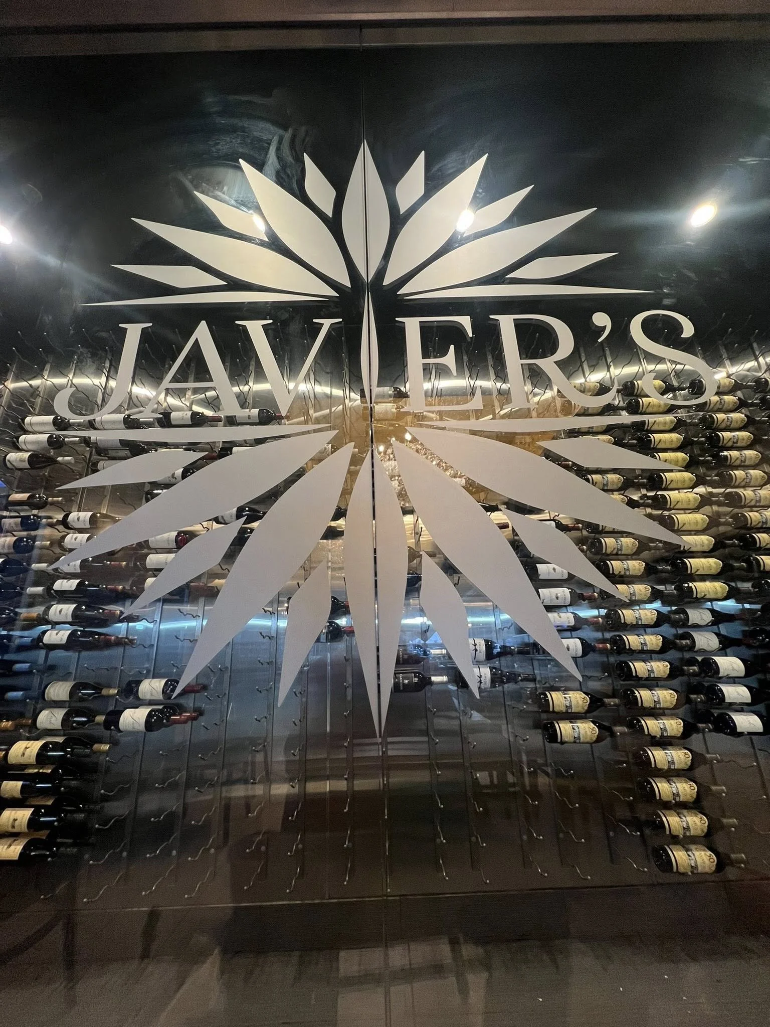 Decorative wine display with a large white starburst logo that says 'JAVIER'S' in front of a wall of wine bottles.