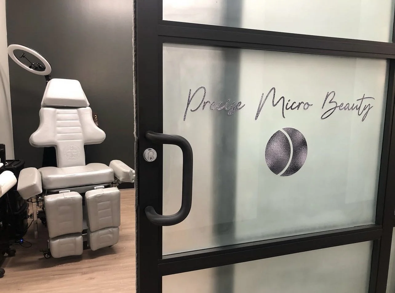 Interior of a micro beauty clinic with a massage or treatment chair and the clinic's door with the sign 'Pulse Micro Beauty' and a logo resembling a stylized eye or oval shape.