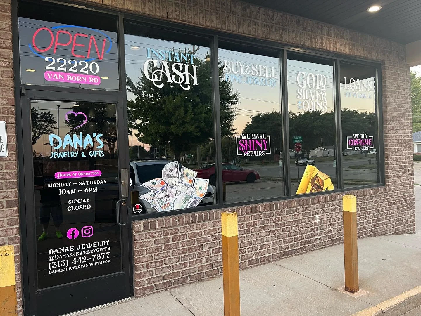 The exterior of Dana's Jewelry & Gifts store featuring neon signs advertising services, a display window with fake dollar bills and jewelry, and informational signs about hours, contact, and social media.