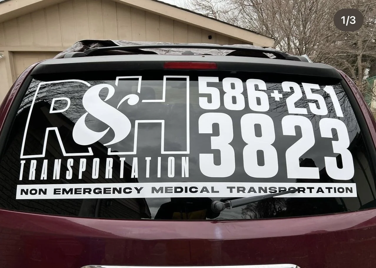 Rear window of a maroon vehicle with white lettering and graphics promoting a transportation service: large text with a phone number, company name, and description reading 'Non Emergency Medical Transportation'.