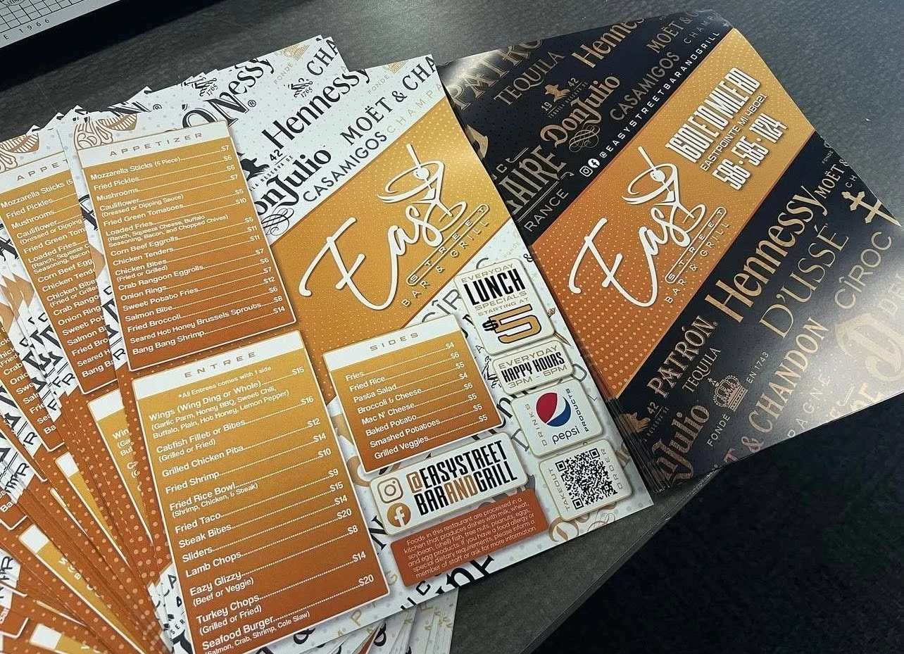 Colorful restaurant menu flyers for Tacos Bar and Grill, featuring sections for appetizers, entrees, sides, and lunch specials, laid out on a dark table.